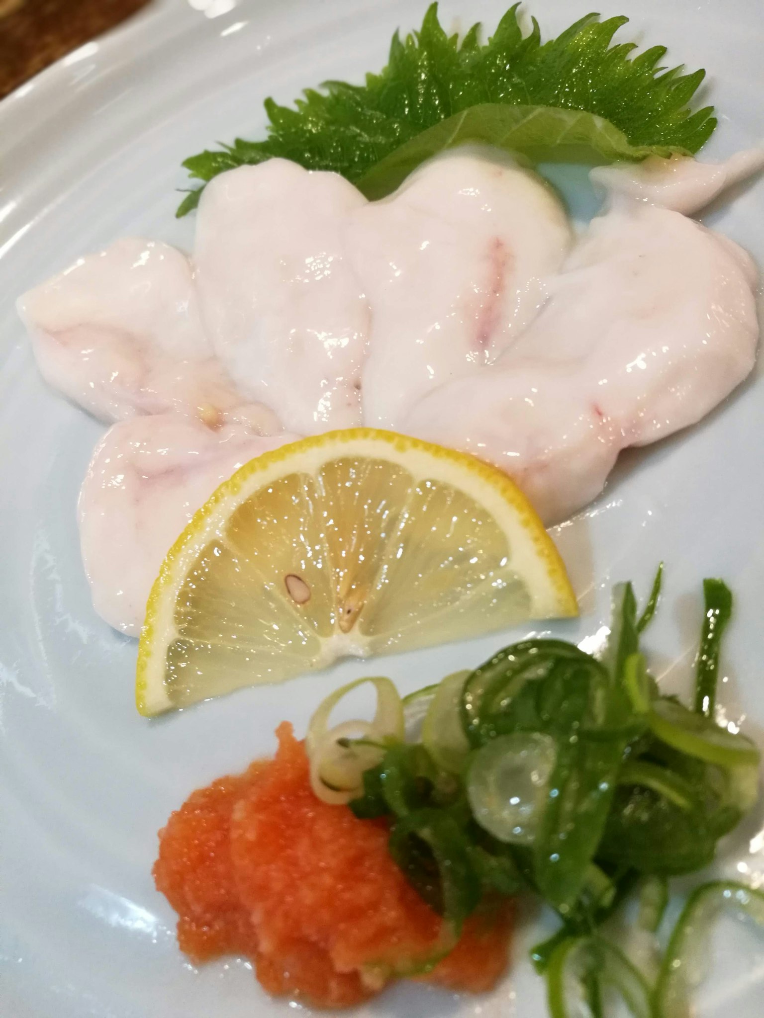 Sashimi ikan putih yang halus dihias dengan lemon dan daun bawang