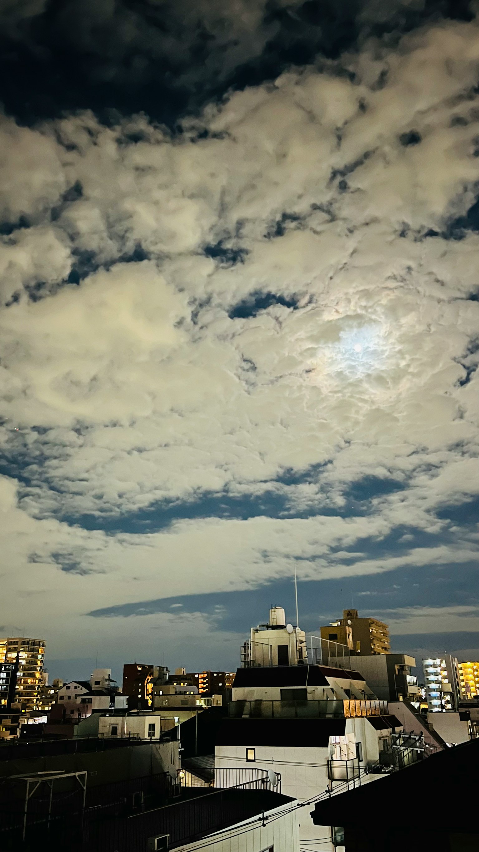 夜空中有雲彩和明亮的月亮在城市屋頂上方