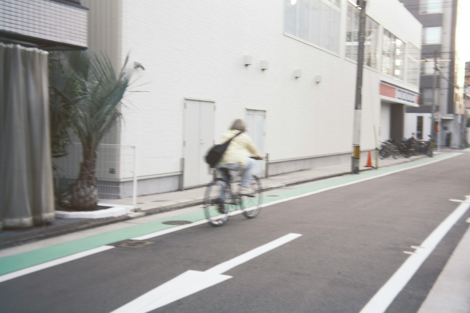 Eine Frau fährt mit dem Fahrrad auf einer städtischen Straße mit einem weißen Gebäude und einem grünen Fahrradweg im Hintergrund