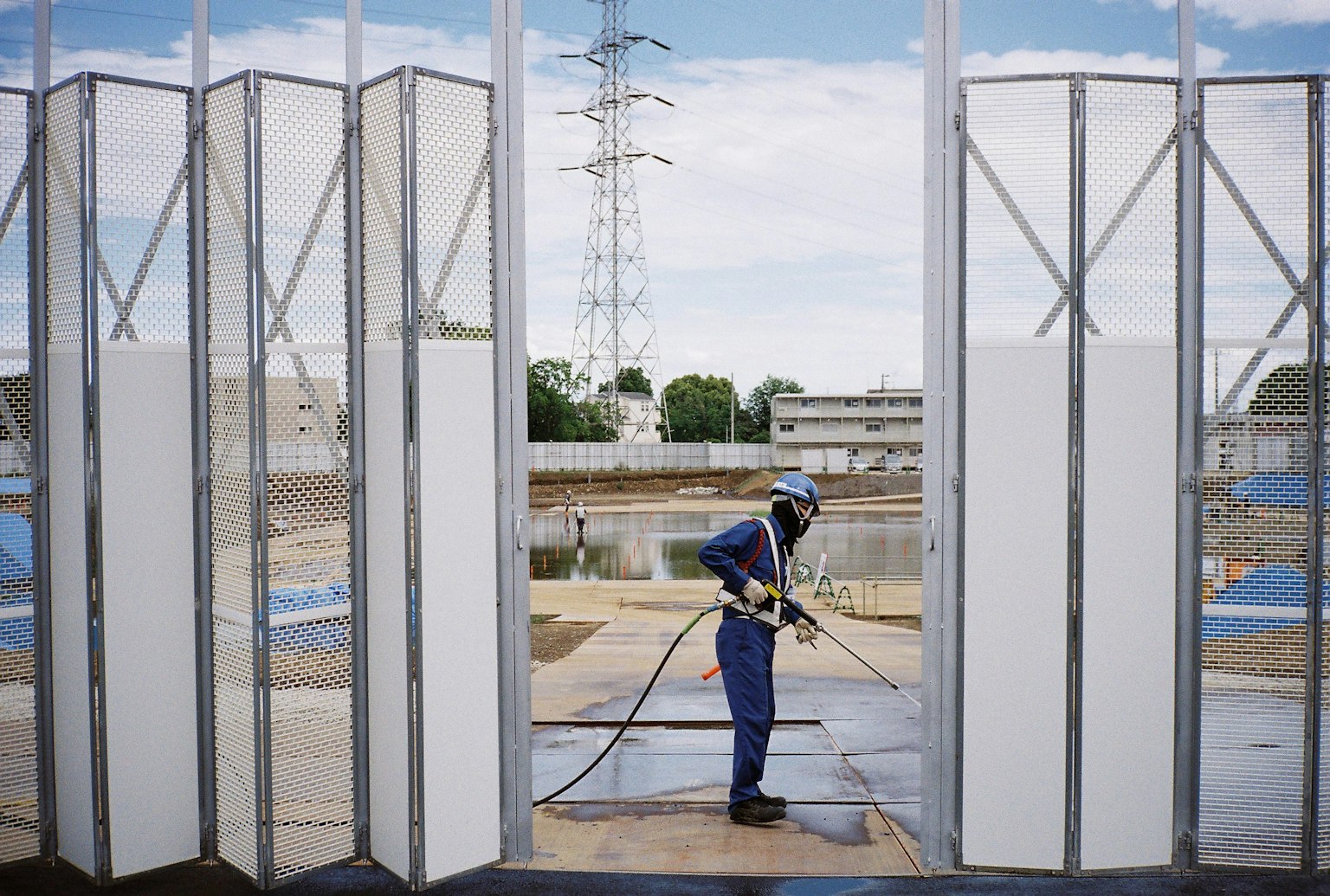 Un lavoratore che utilizza un idropulitrice in un cantiere con pannelli di vetro e linee elettriche sullo sfondo