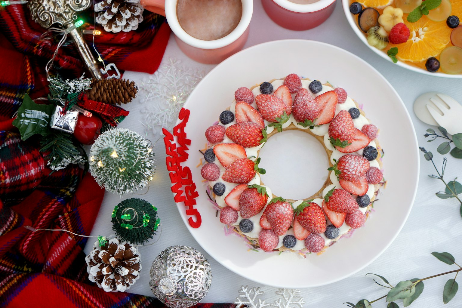 크리스마스 디저트 배열로 중앙에 딸기와 블루베리로 장식된 케이크가 놓여 있다