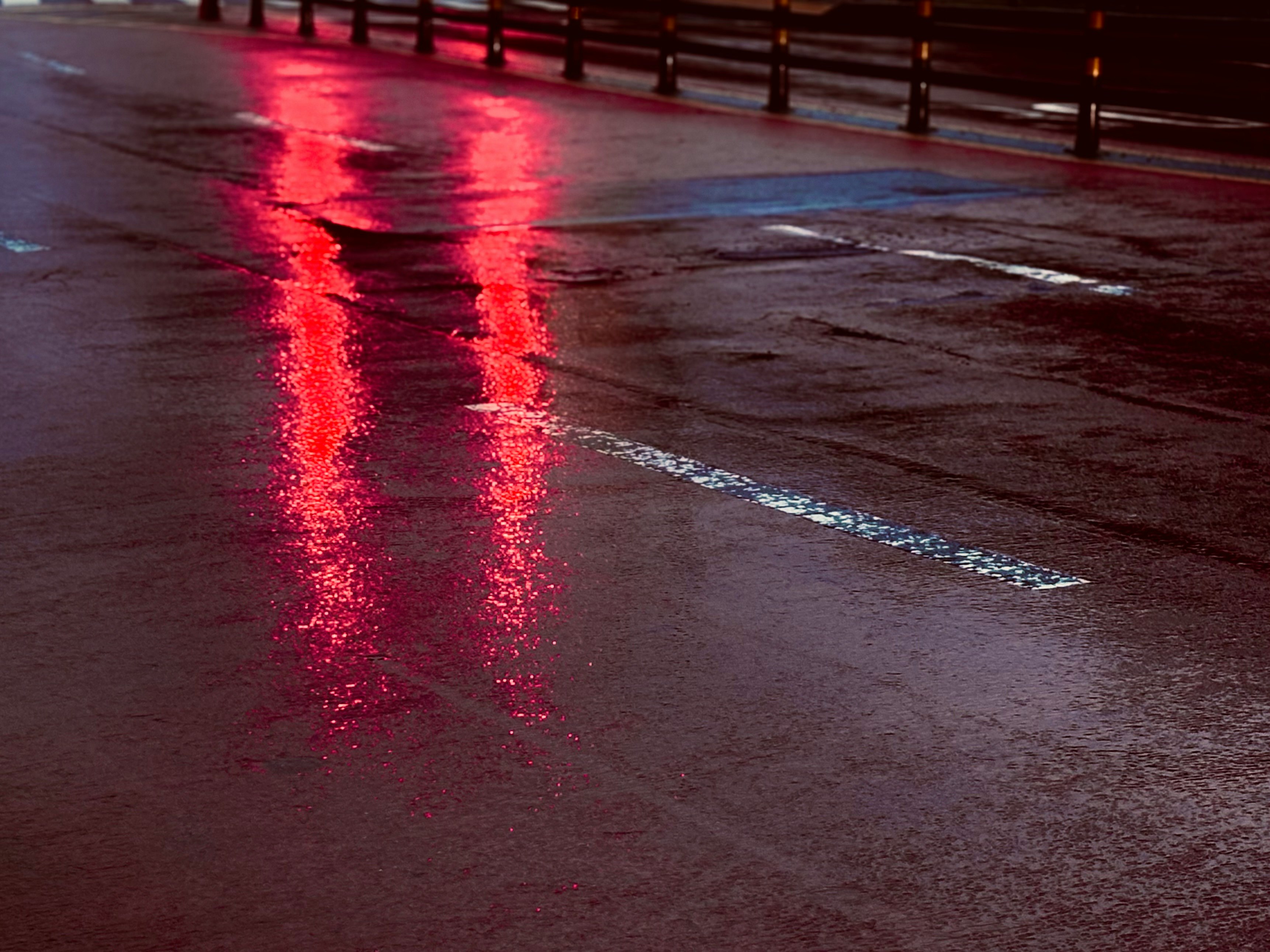 雨上がりの濡れた道路に伸びる赤い反射光