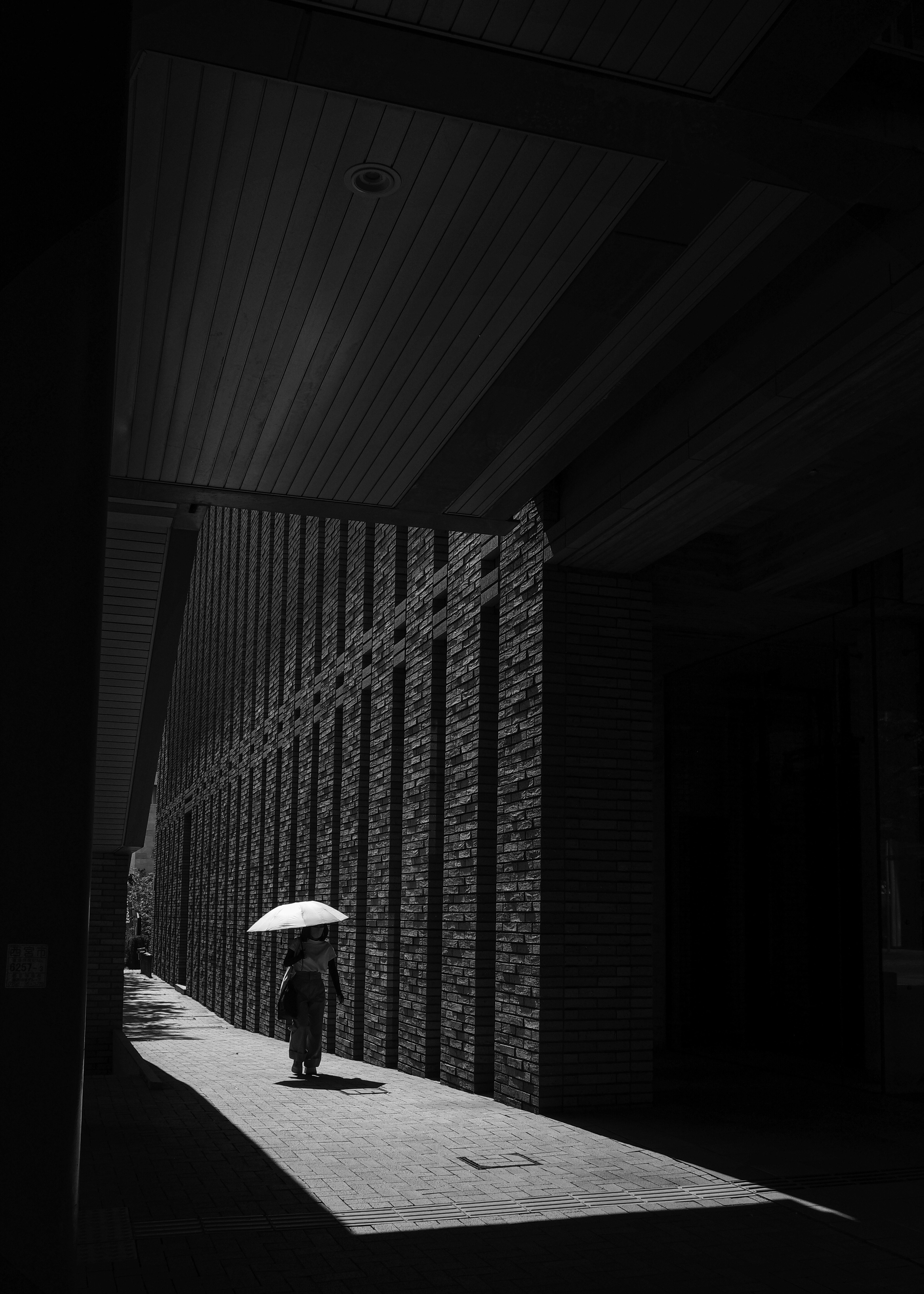 Scène de rue monochrome : une personne avec un parapluie sous la pluie, lumière et ombres