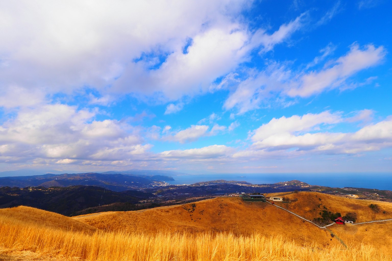 Weite Landschaft mit trockenen Gras-Hügeln unter einem blauen Himmel und weißen Wolken
