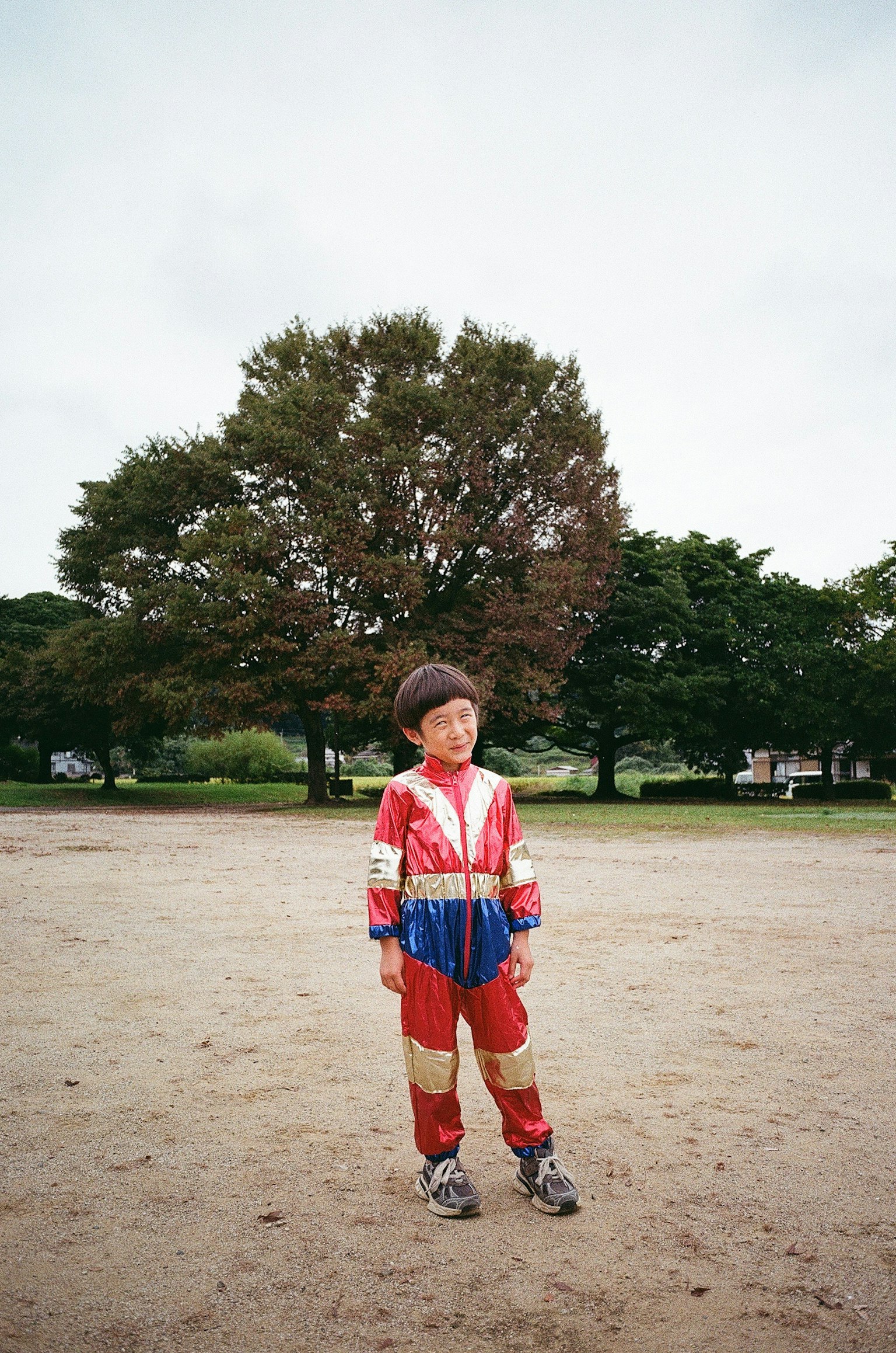 赤と青のスーツを着た子供が公園で立っている背景には大きな木がある
