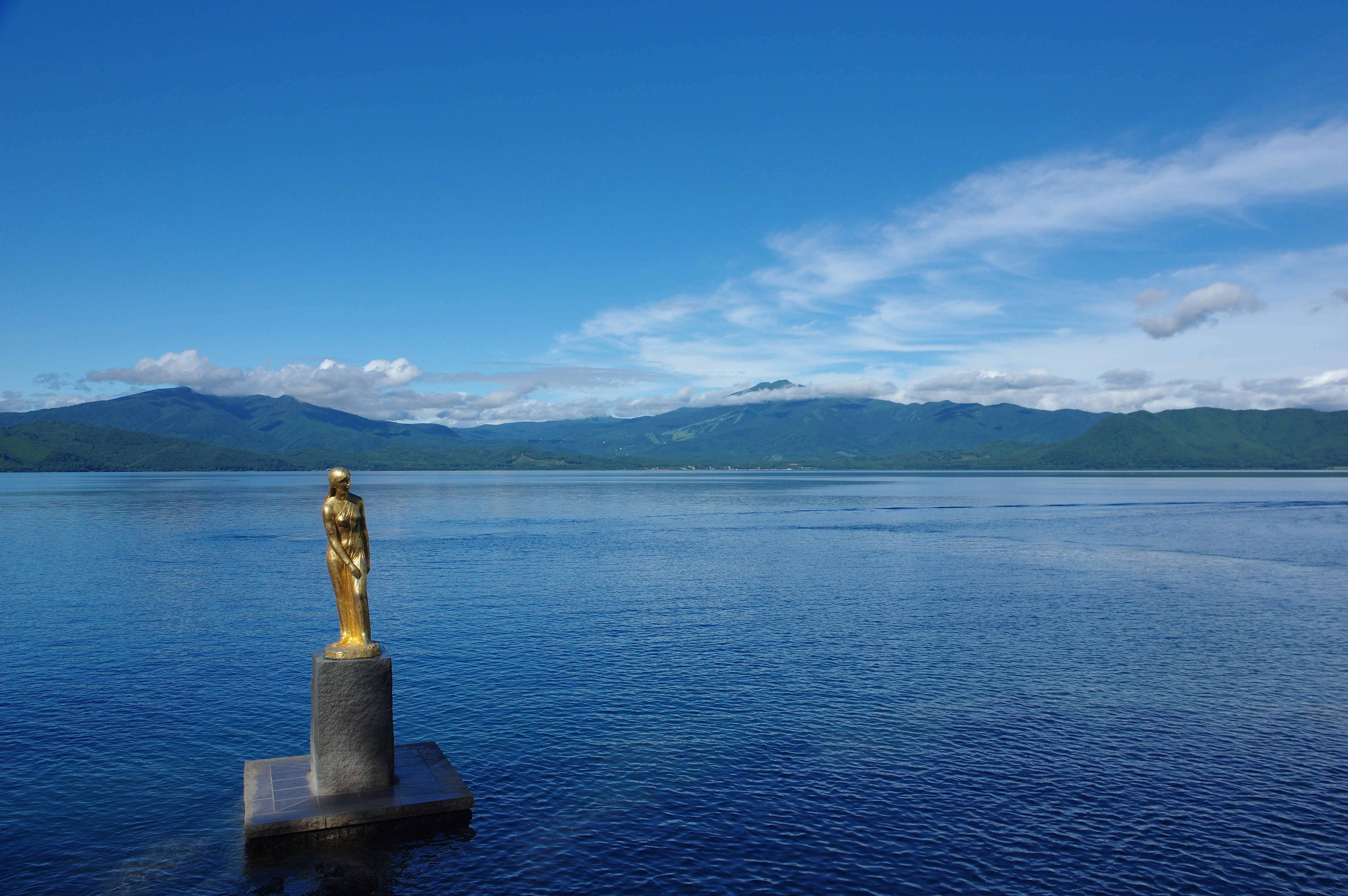 patung emas di atas alas di tepi danau dengan hamparan air yang luas