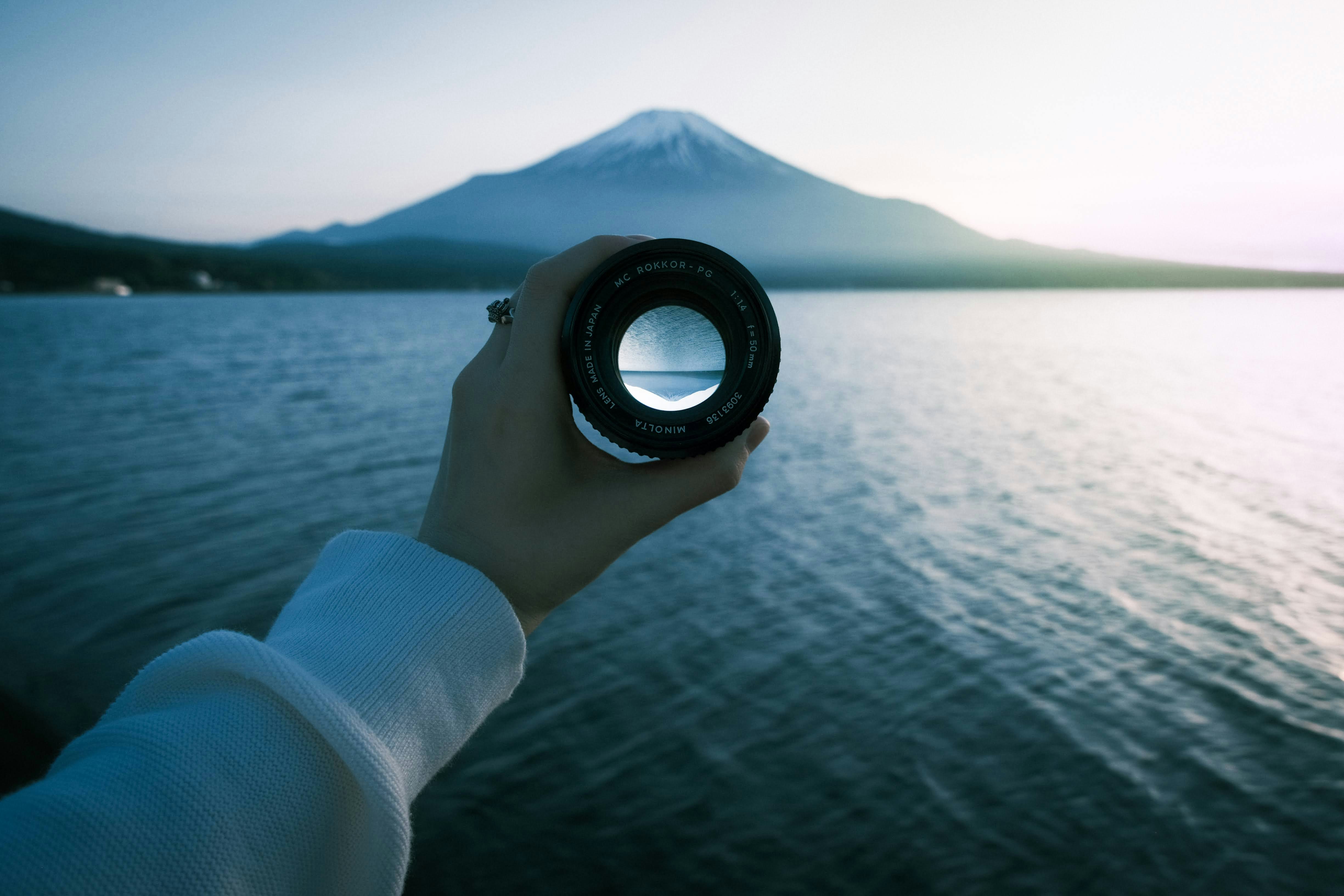 Hand holding a telescope by a lakeside at dusk with a mountain in view