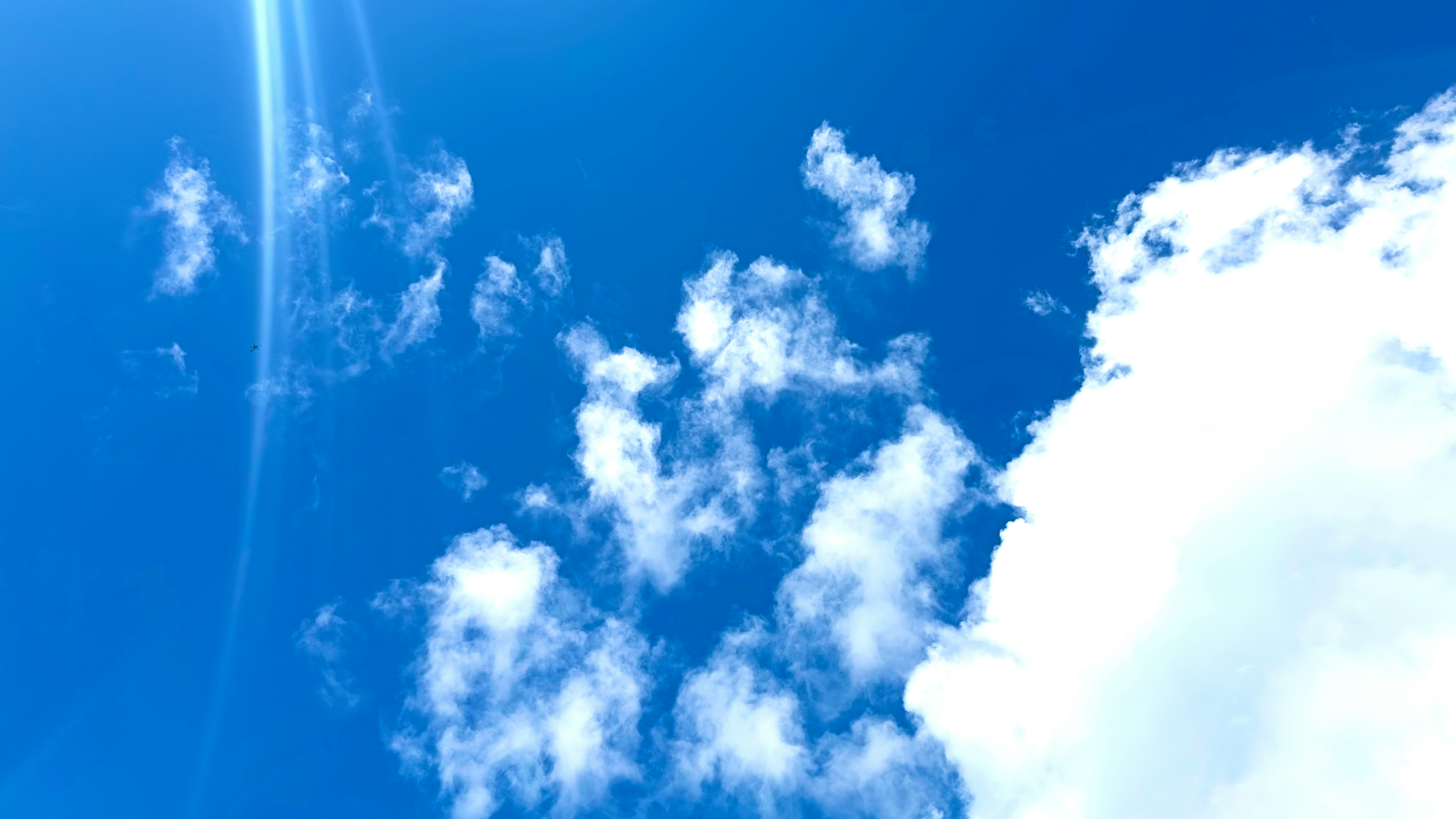 青空に浮かぶ白い雲と光の筋のある空の風景