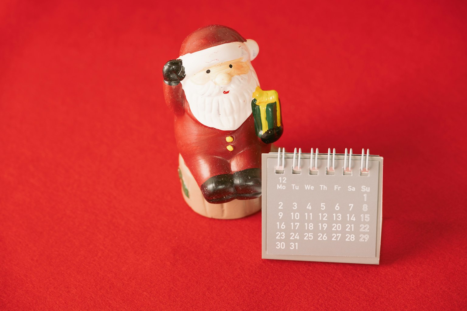 Patung Santa Claus di samping kalender di latar belakang merah