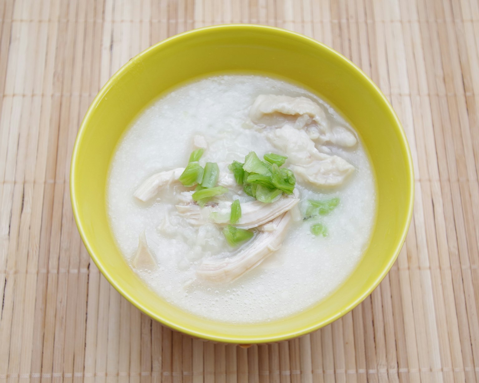 Congee di pollo servito in una ciotola gialla con cipollotti verdi
