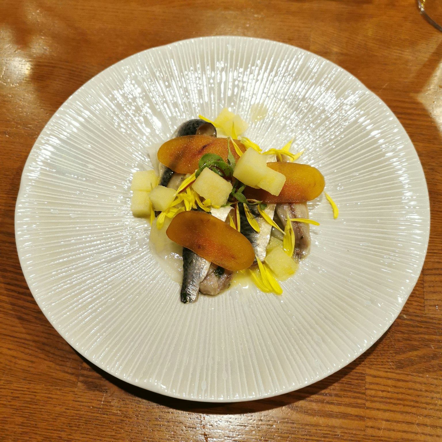 A beautifully presented fish dish on a white plate with fresh vegetables and flower garnishes