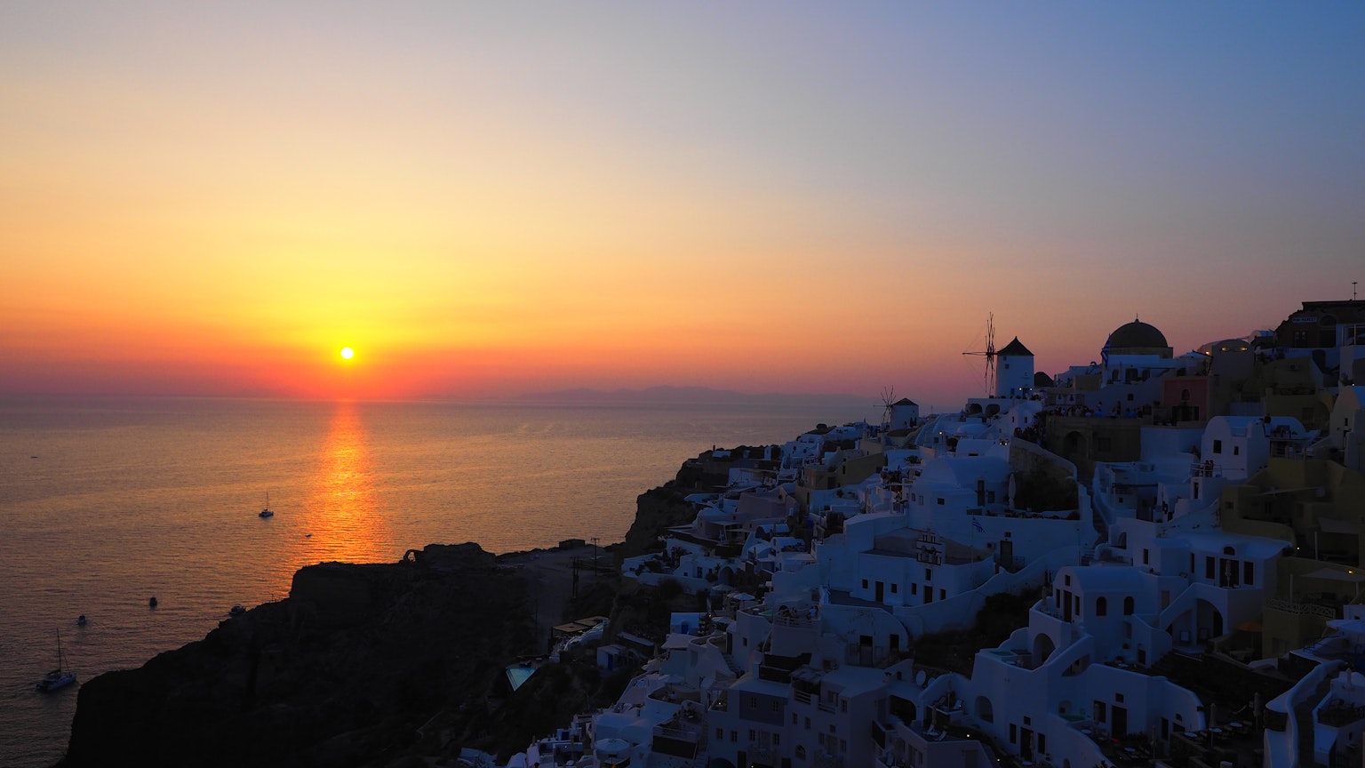 Beeindruckender Sonnenuntergang über Santorin mit weißen Gebäuden und ruhigem Meer
