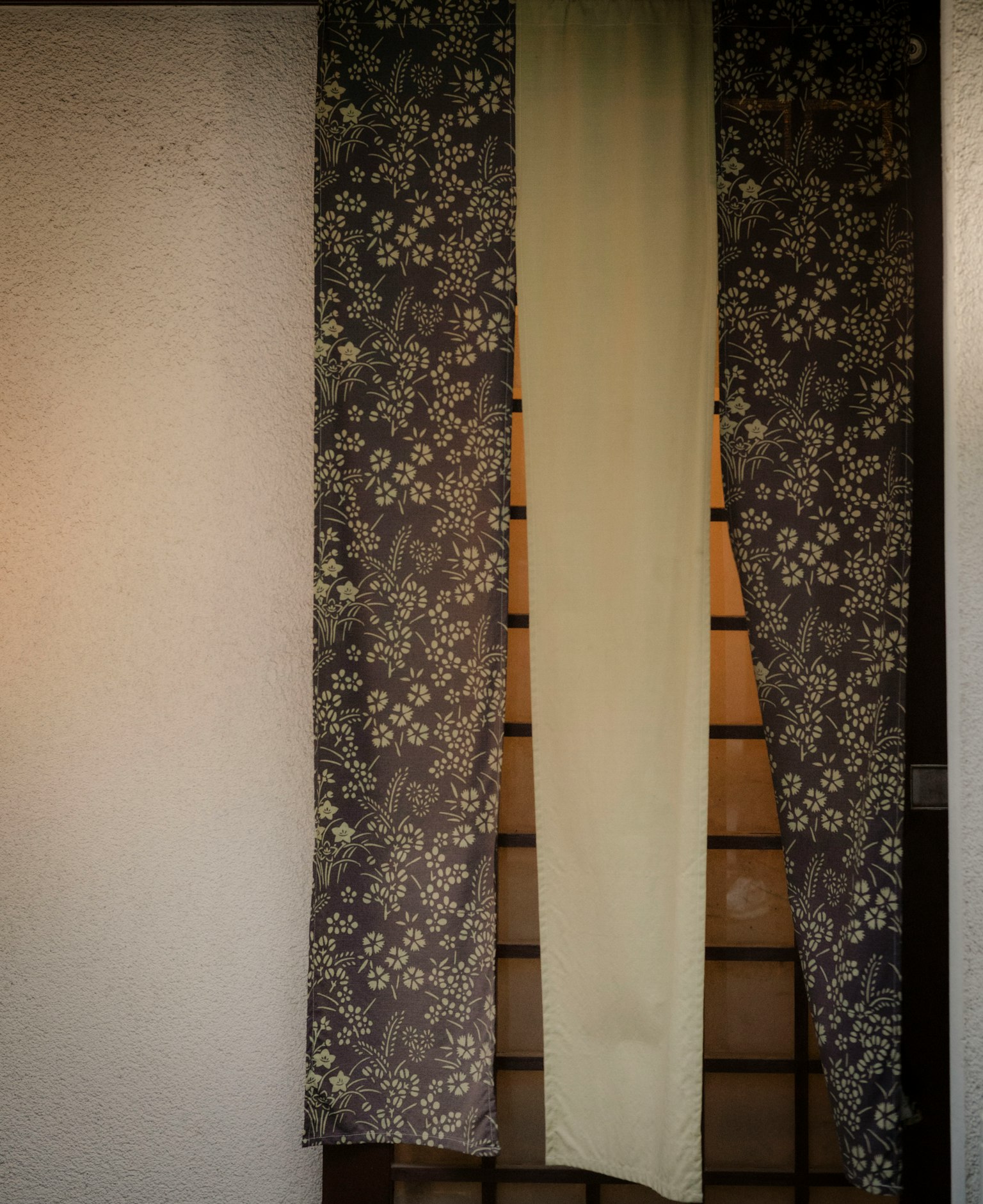 和風のカーテンが掛かる部屋の入り口の画像 花柄のカーテンと淡い色の布が特徴的
