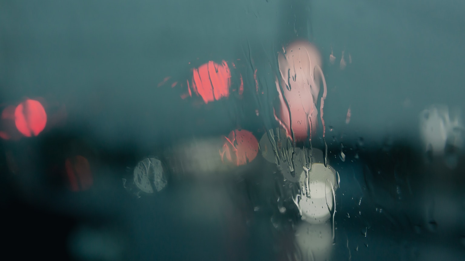 Luces borrosas y círculos coloridos vistos a través de la lluvia en el vidrio