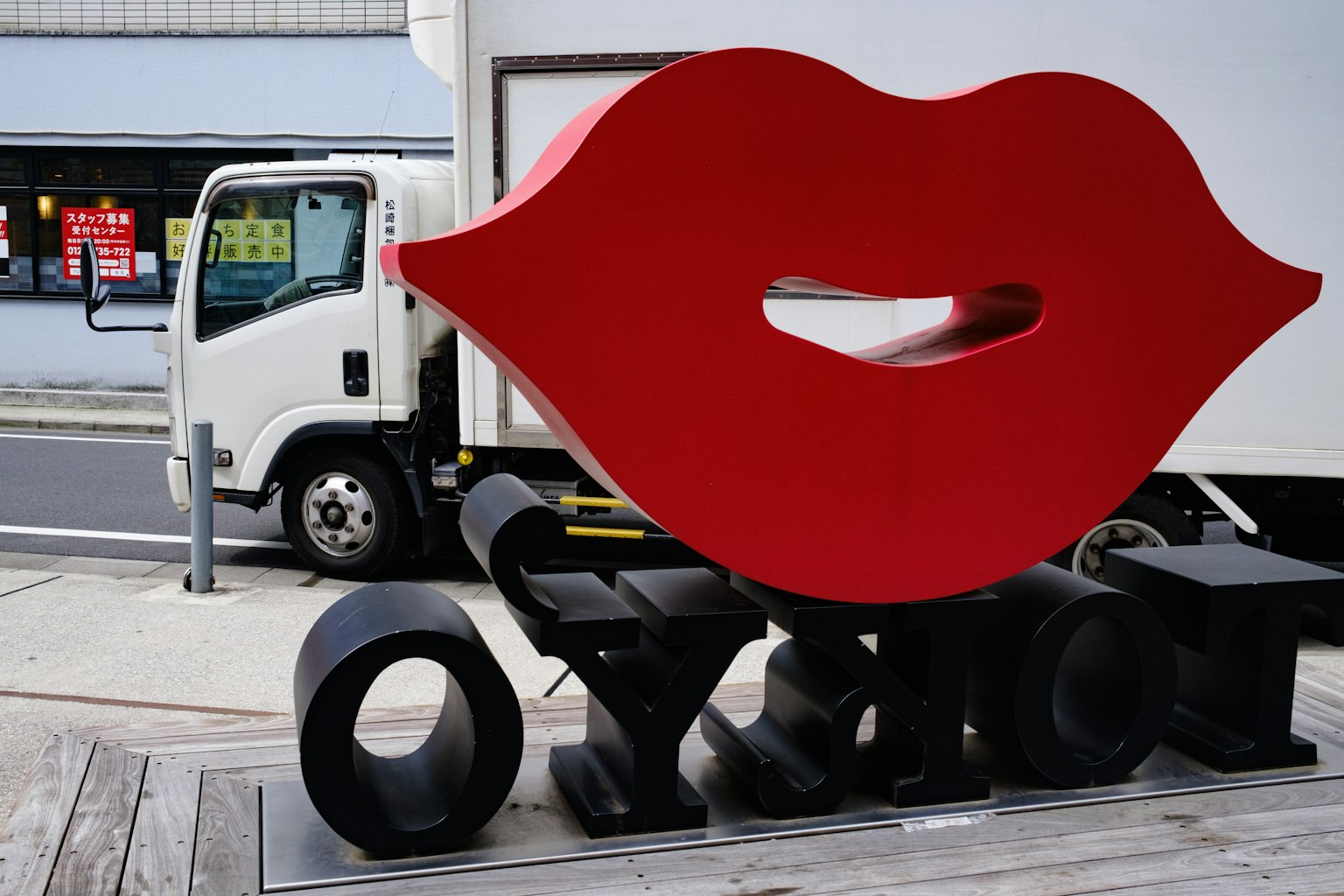 Scultura di labbra rosse in un contesto urbano con un camion sullo sfondo