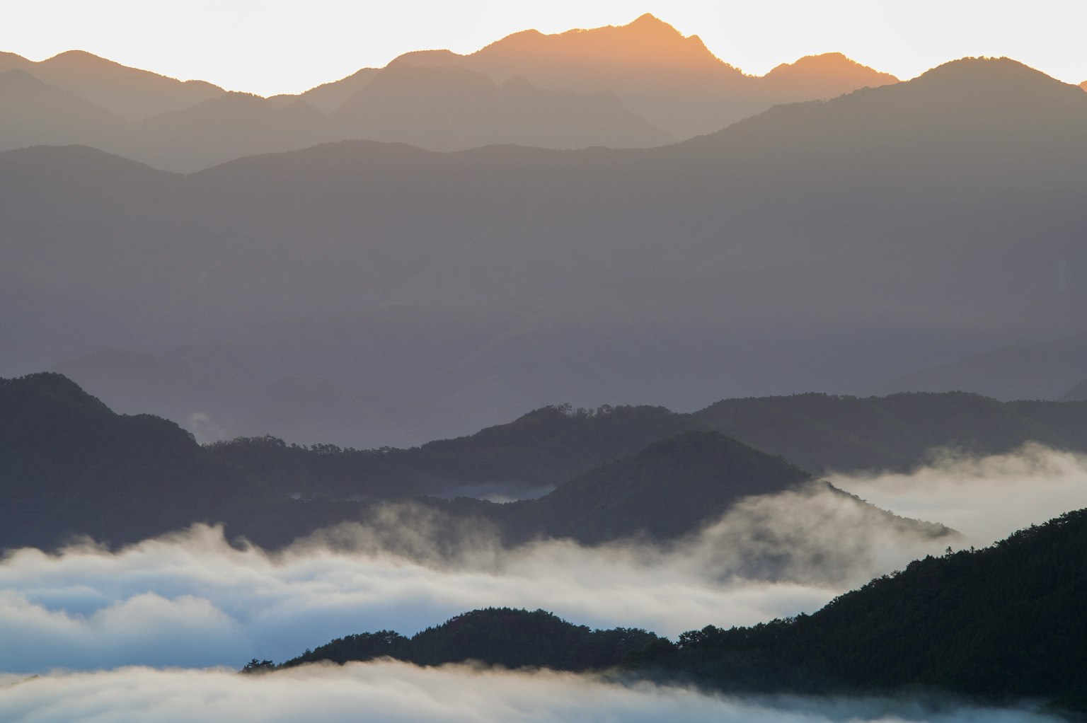 Montagne in silhouette avvolte nella nebbia con riflessi dell'alba
