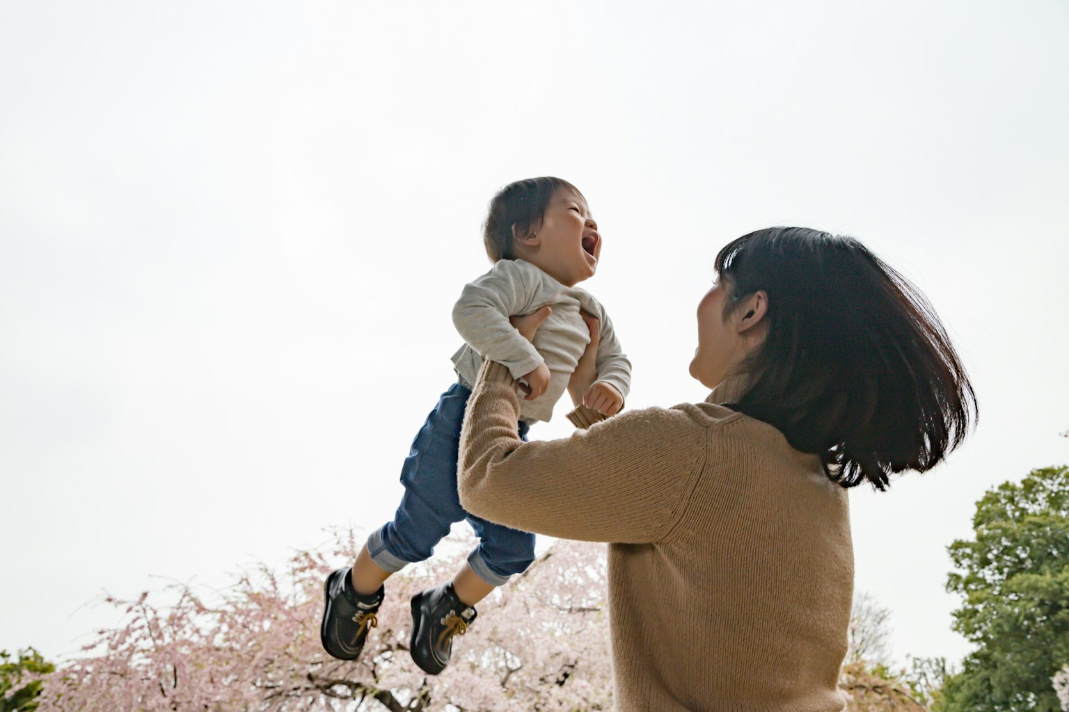 A mother lifting her child under a cherry blossom tree