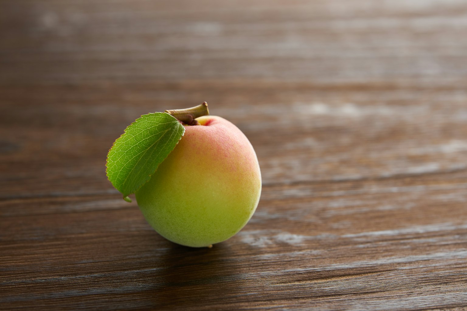 A green and red apple resting on a wooden table