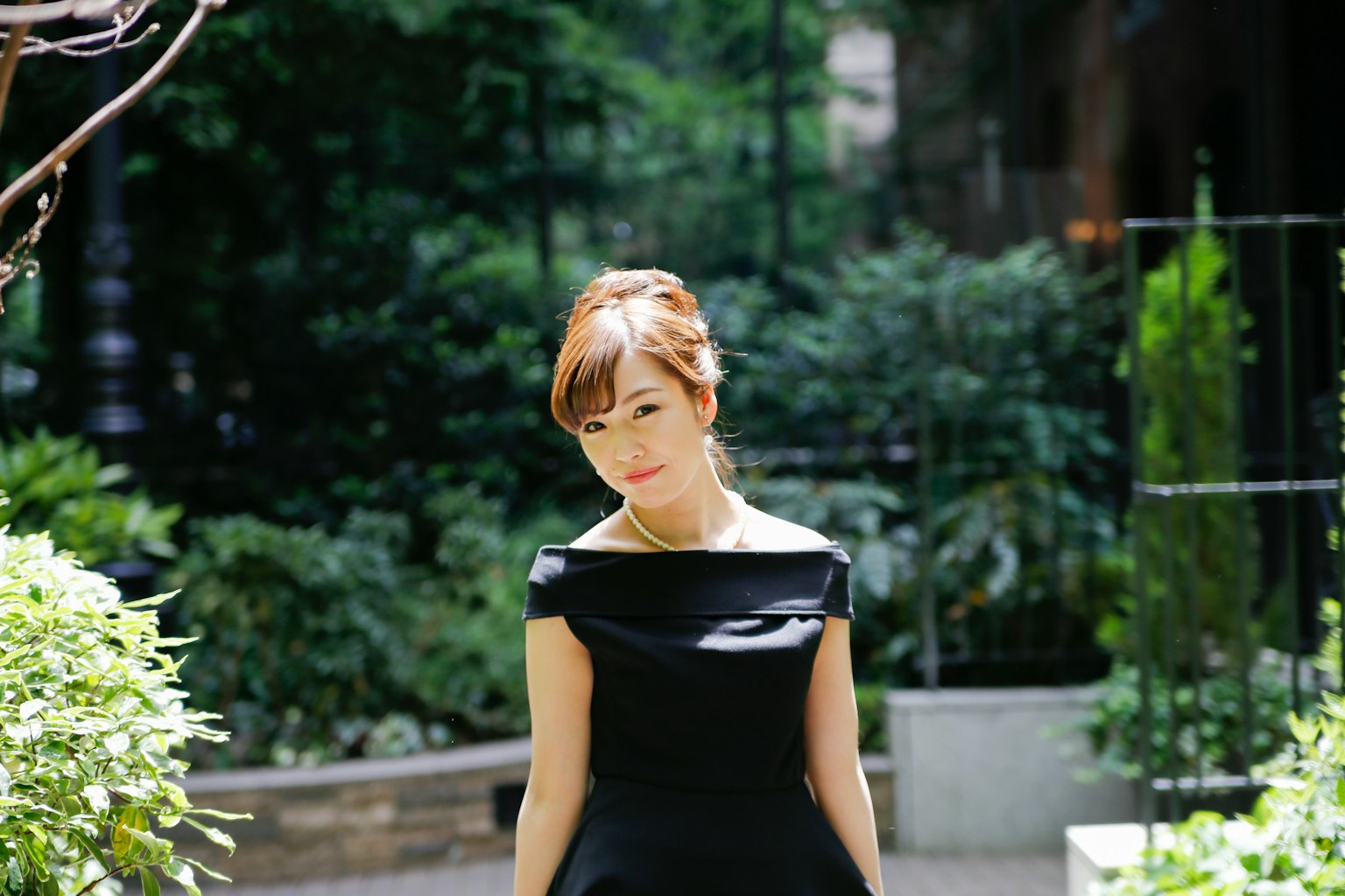 검은 드레스를 입은 여성이 정원에서 걷고 있다