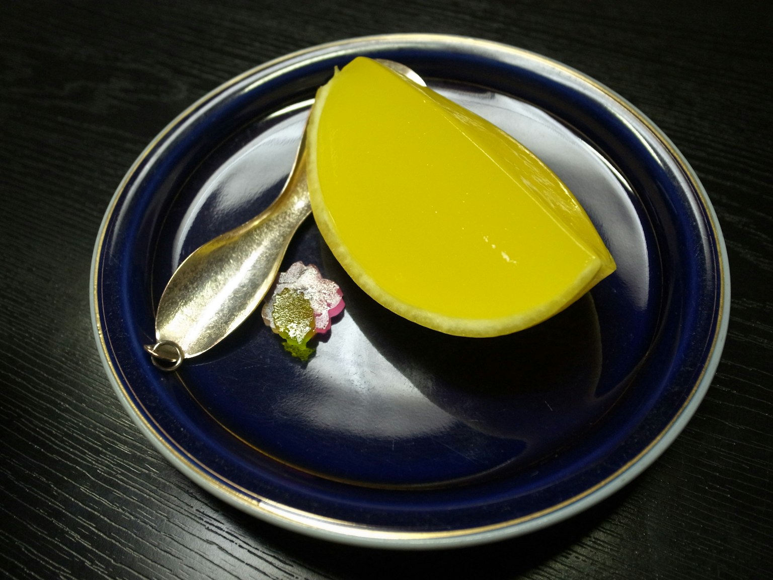 Dessert giallo servito su un piatto blu con un cucchiaio d'argento e guarnizione decorativa