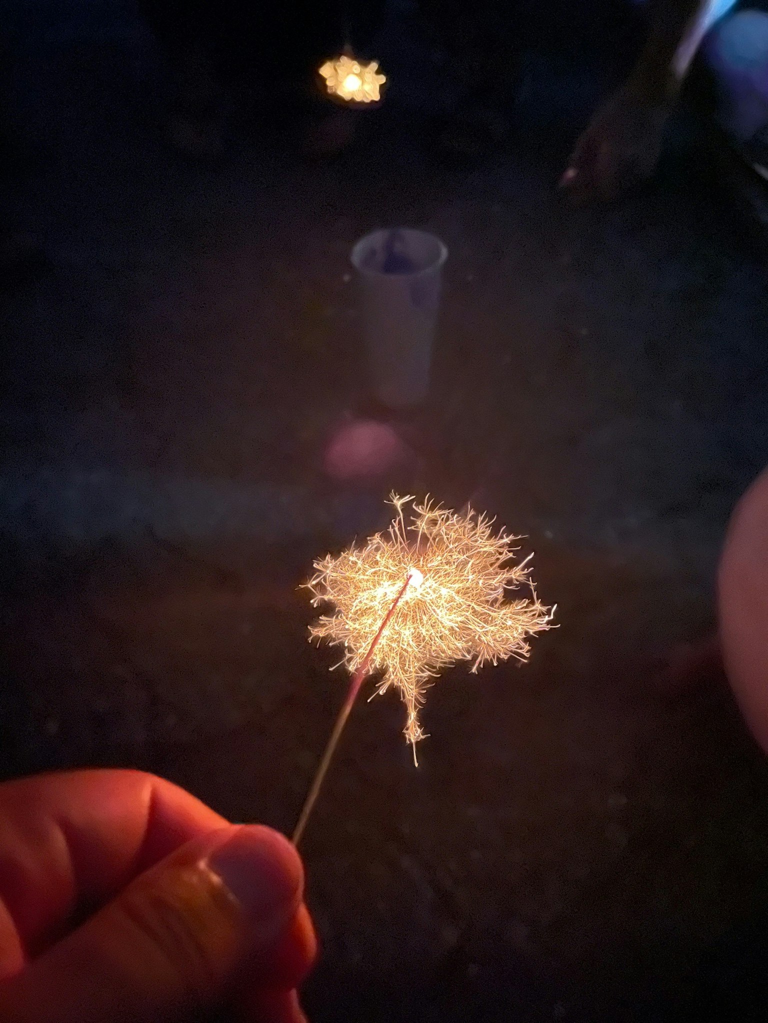 A hand holding a sparkling firework against a dark background