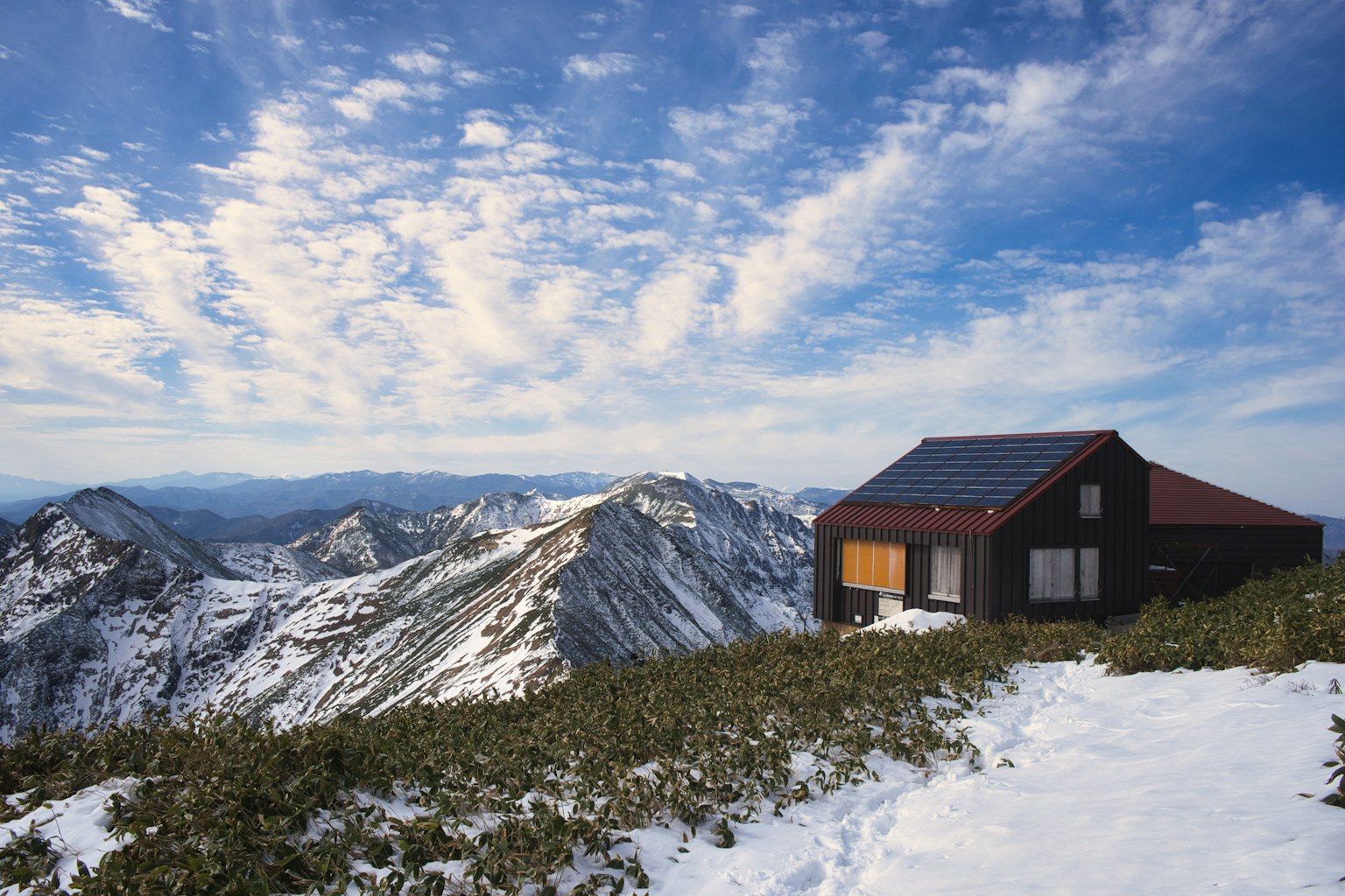 Una cabaña negra rodeada de picos cubiertos de nieve y un cielo azul