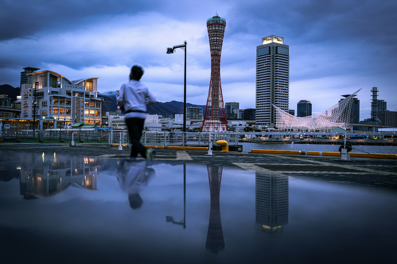 Silhouette einer Person, die mit dem Kobe Port Tower und der Stadtsilhouette im Hintergrund geht