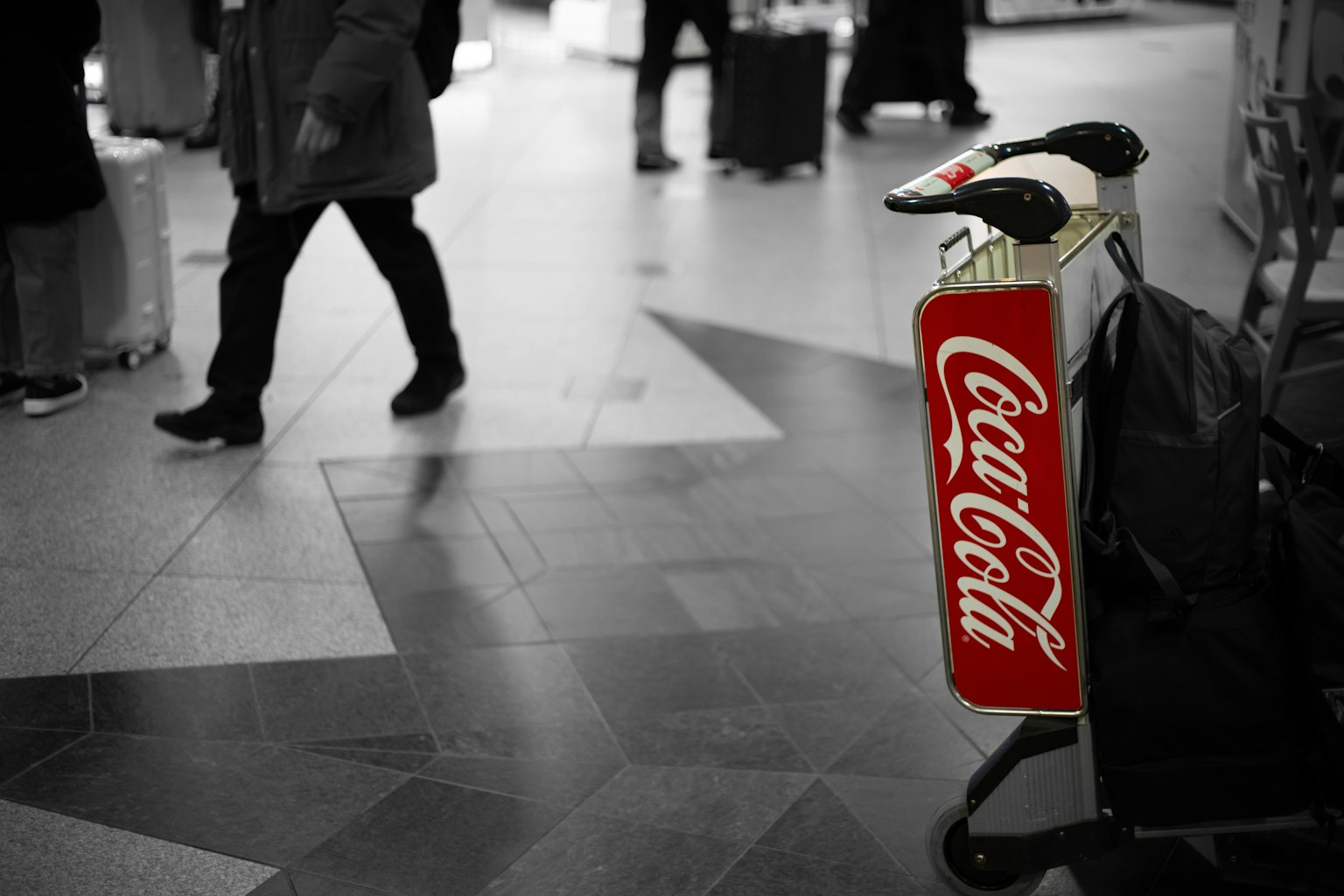Una scena in bianco e nero con un cartello rosso della Coca-Cola in primo piano in una stazione