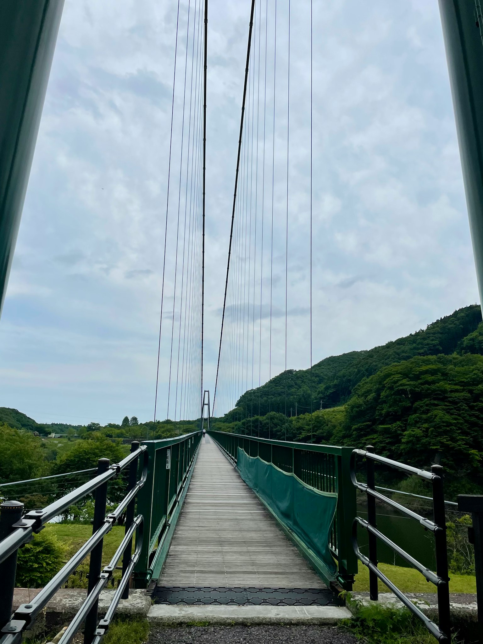 Ponte sospeso circondato da colline verdi con cielo e sentiero visibili