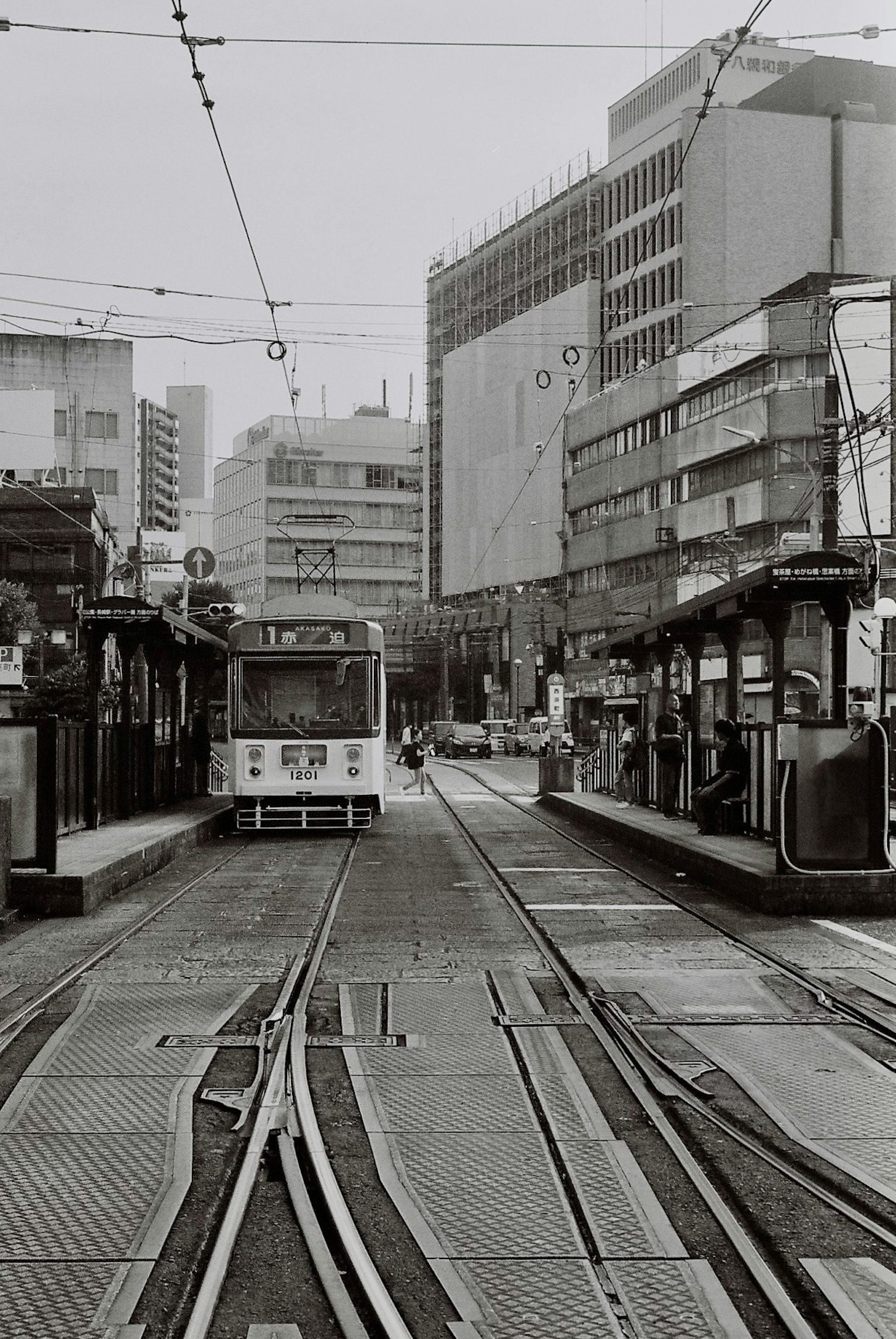 Scène de rue en noir et blanc avec un tram et une station
