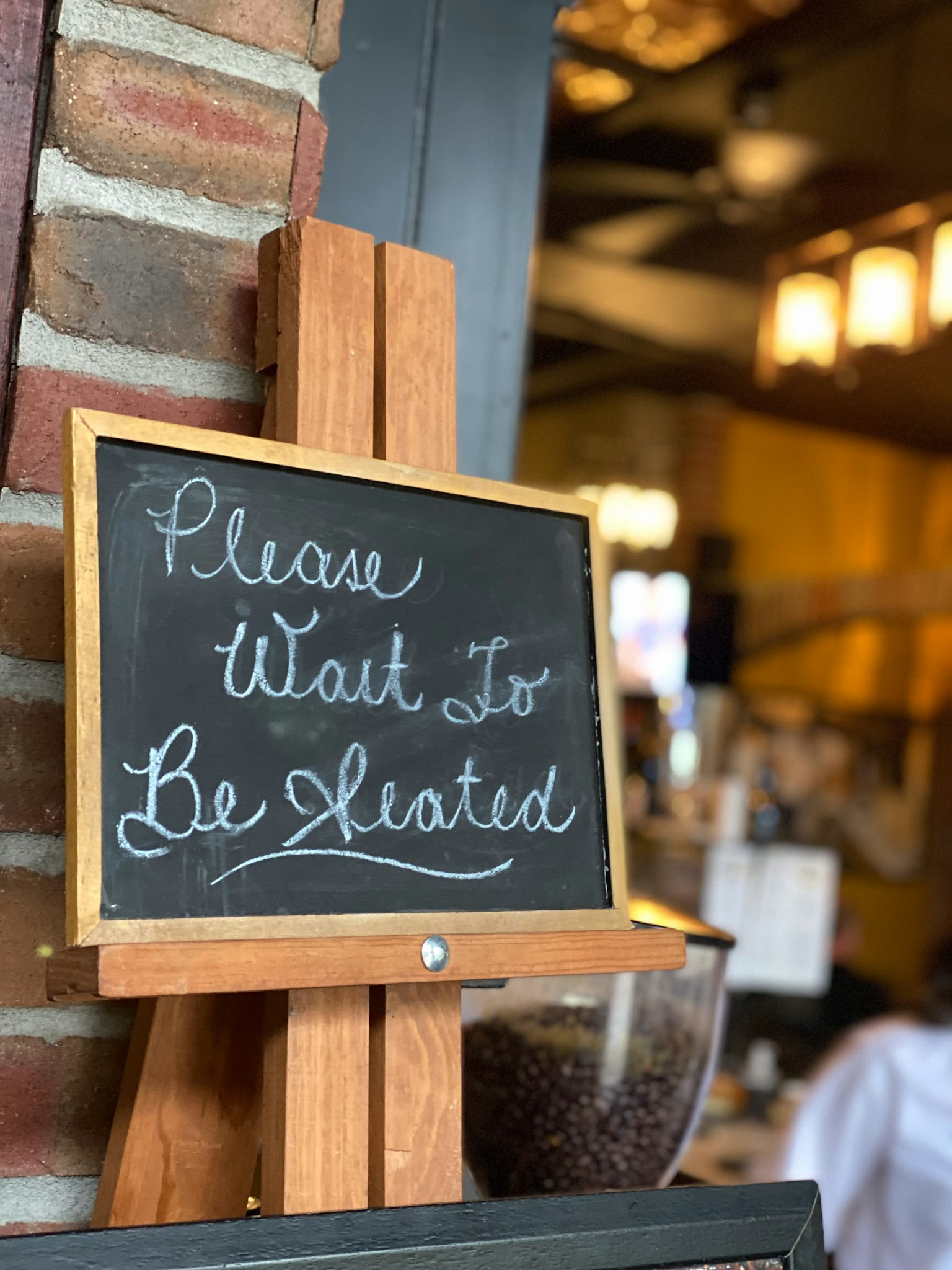 Chalkboard sign at a restaurant entrance saying Please Wait to Be Seated