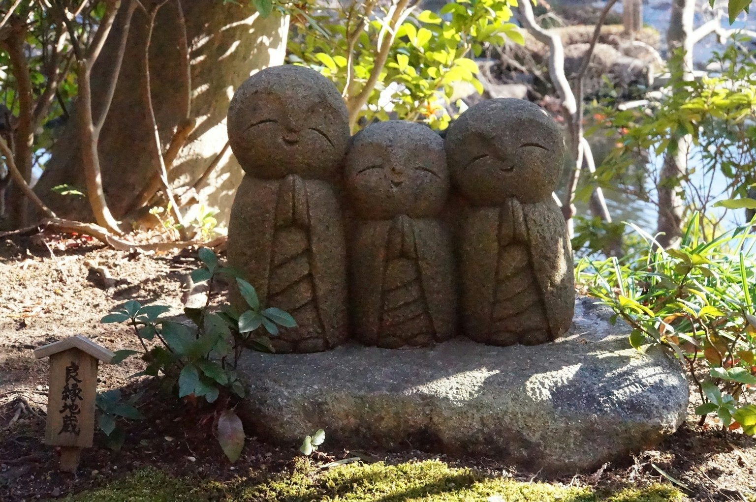 Tres pequeñas estatuas de piedra de pie juntas en un jardín