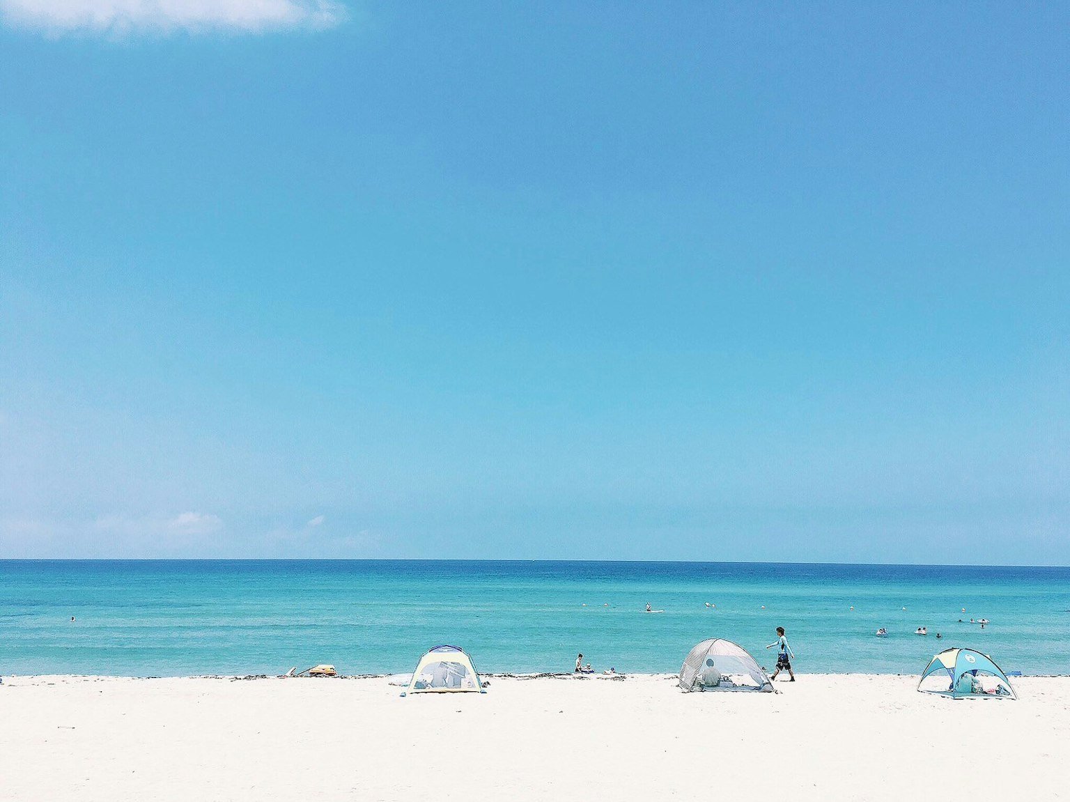 คนยืนอยู่บนชายหาดที่มีมหาสมุทรสีน้ำเงินและทรายขาว