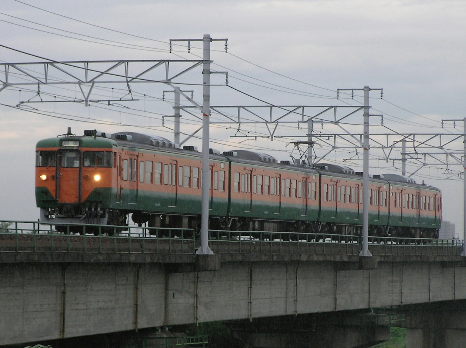 橙色和綠色的火車在高架軌道上行駛