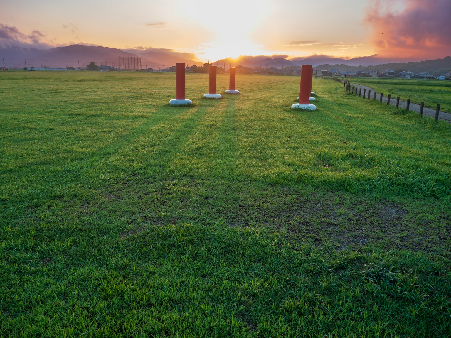 Red pillars standing in a grassy field at sunset with mountains in the background