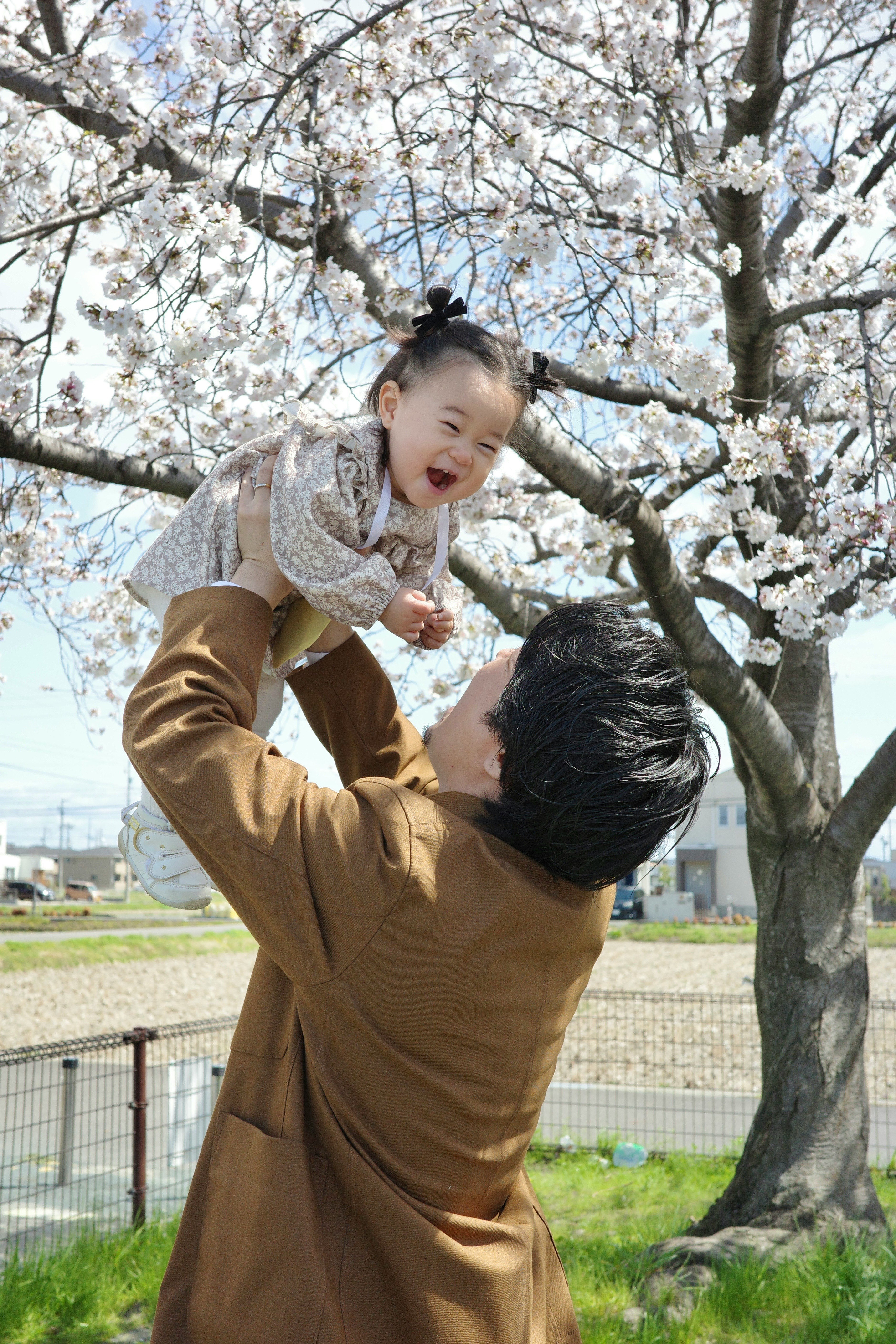 桜の木の下で子どもを抱き上げる親子の入園風景