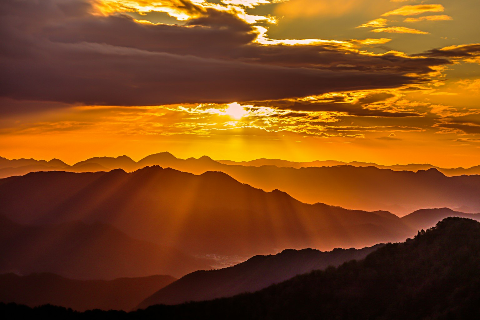 Silhouetten von Bergen vor einem lebhaften orangefarbenen Sonnenuntergangshimmel