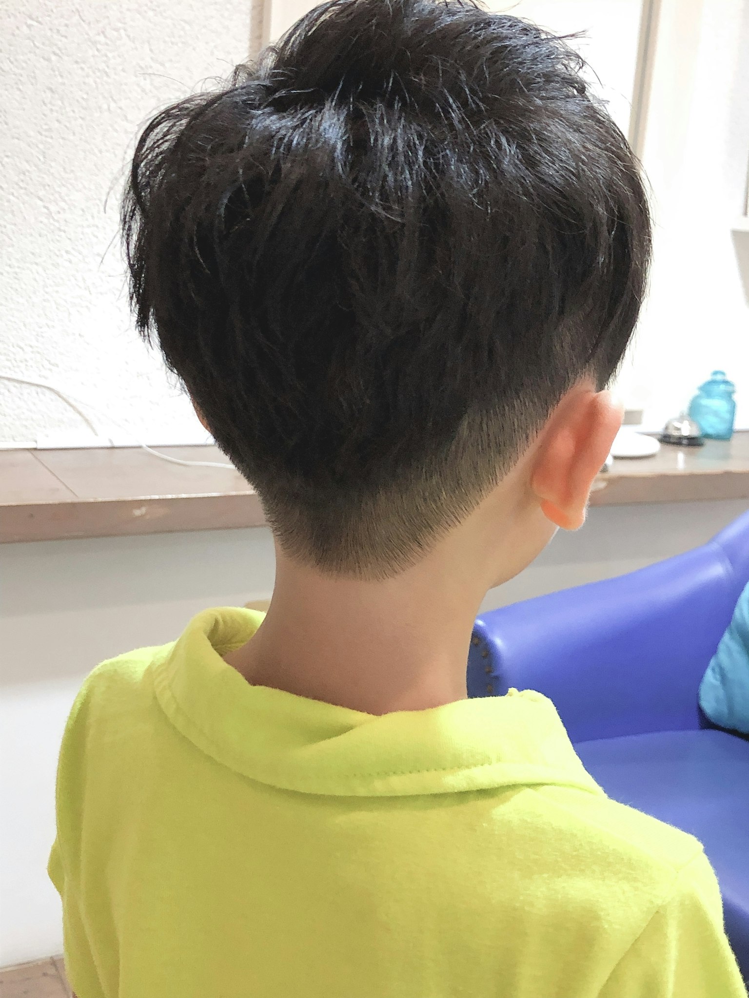 Hình ảnh từ phía sau của một cậu bé với kiểu tóc ngắn mặc áo phông màu vàng sáng