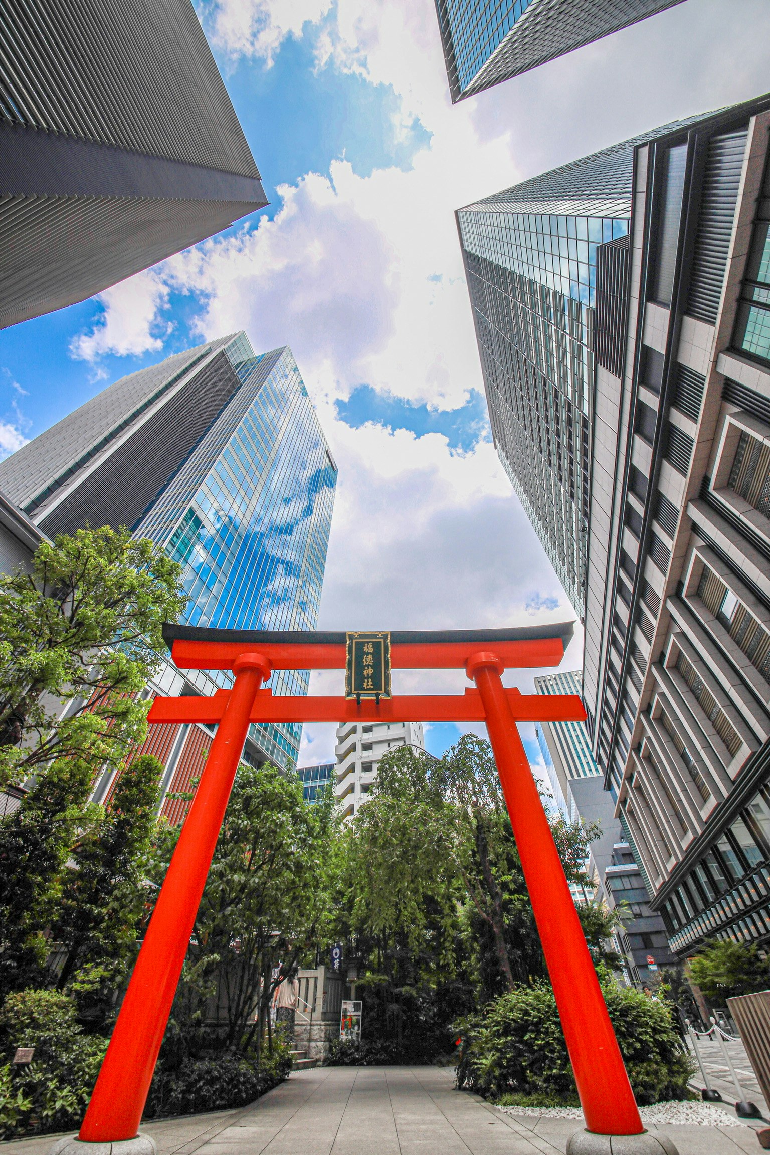 Red torii gate surrounded by skyscrapers and blue sky