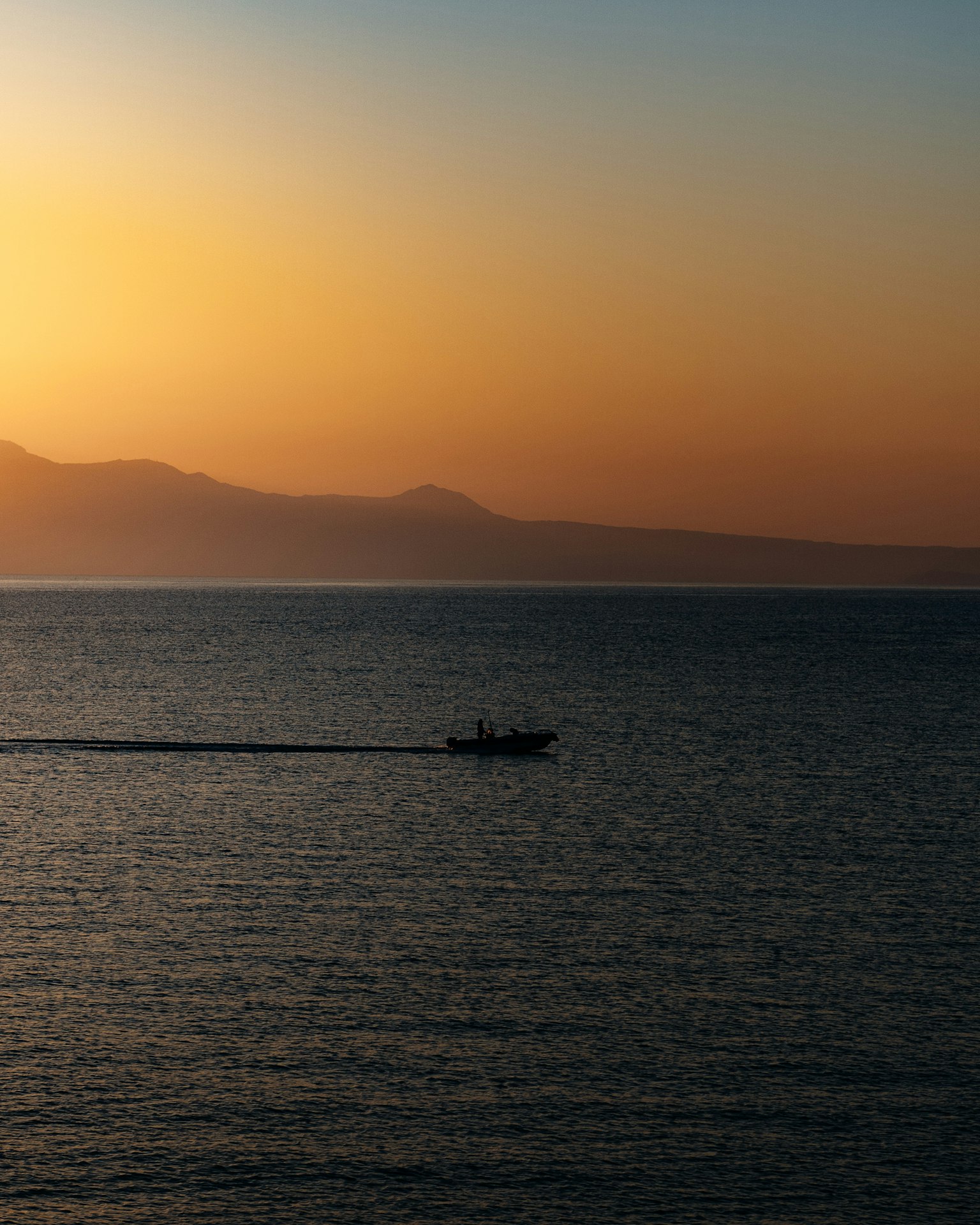 Un petit bateau sur une mer au coucher de soleil avec des montagnes au loin