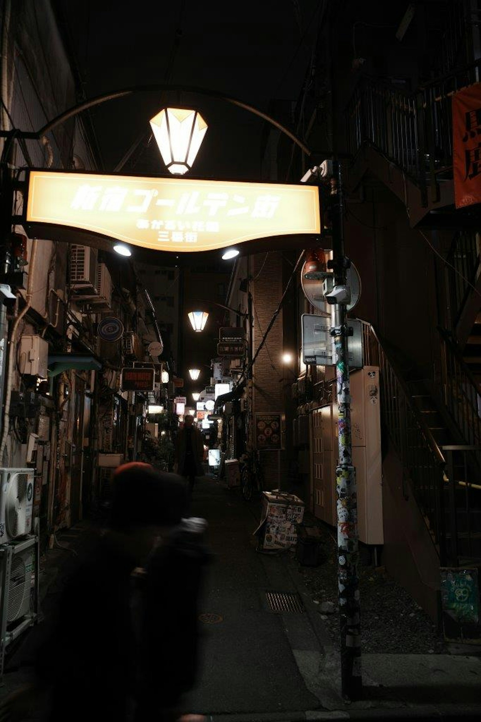 A nighttime alley with a bright sign and street lamps