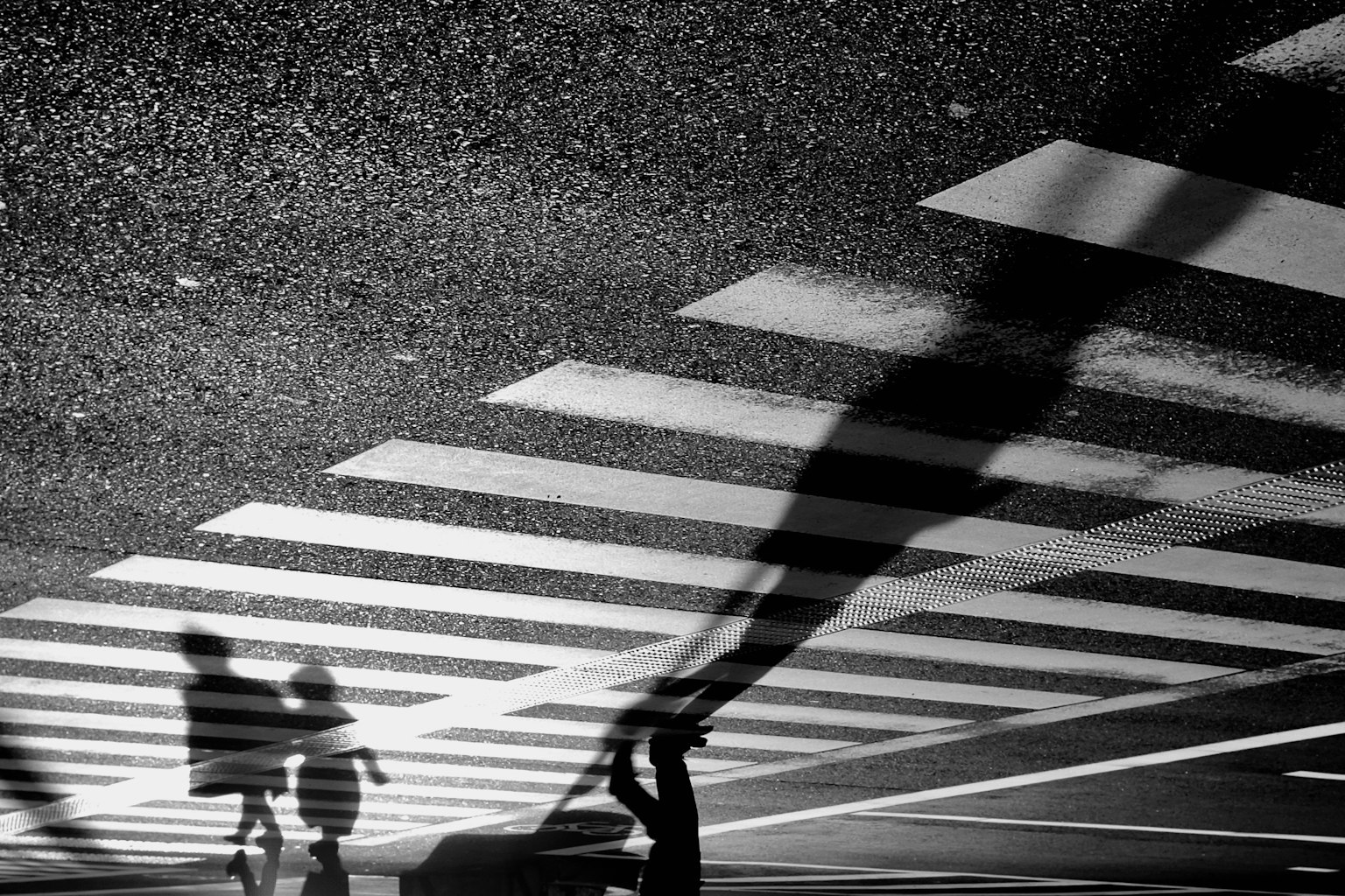 Shadows of people crossing a black and white crosswalk