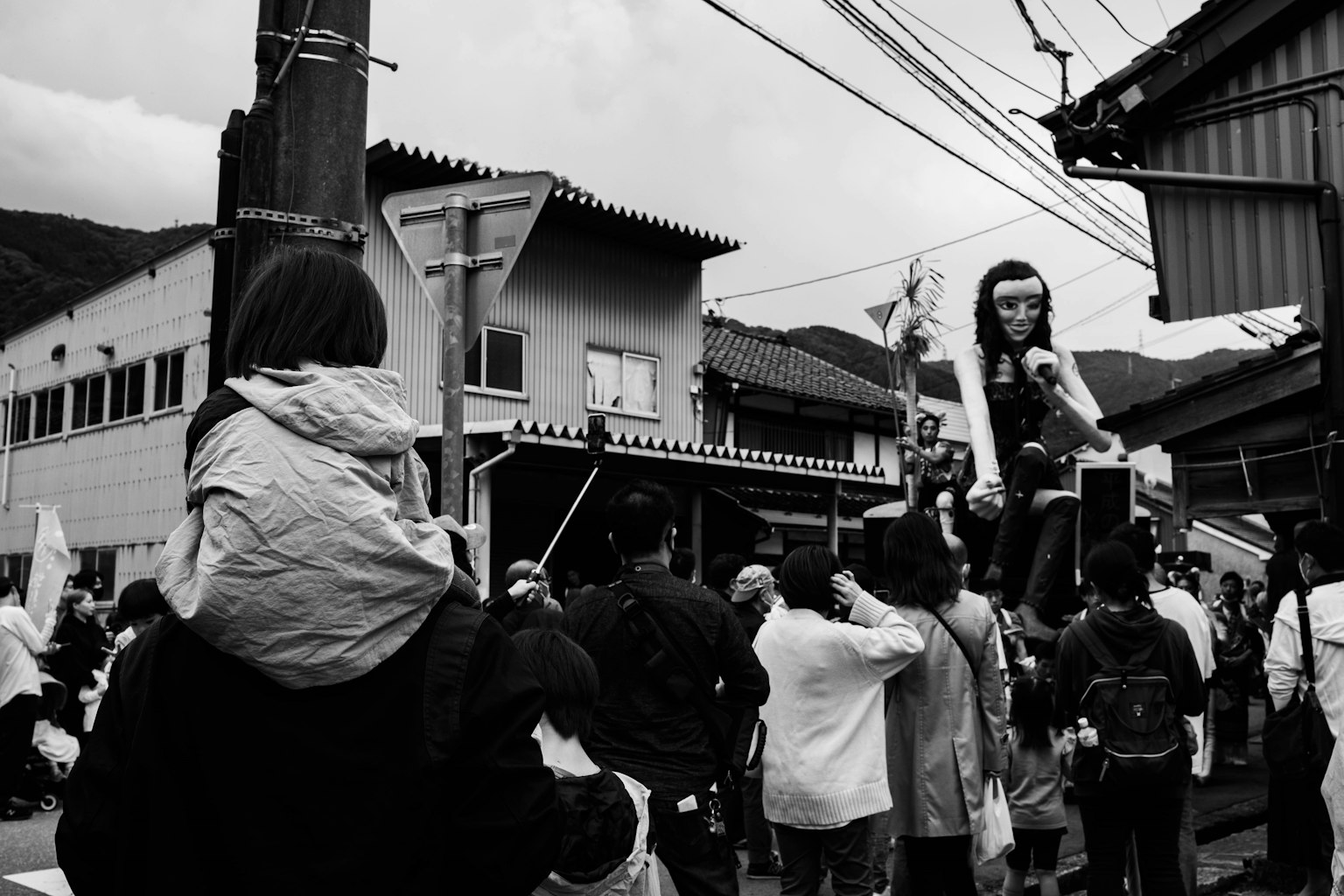 Multitud reunida en un festival callejero en blanco y negro con edificios y líneas eléctricas