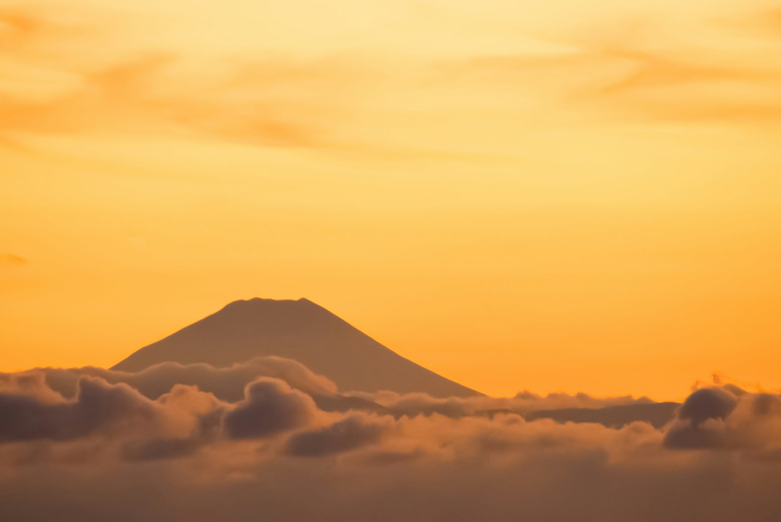 Mont Fuji silhouetté contre un coucher de soleil doré au-dessus des nuages