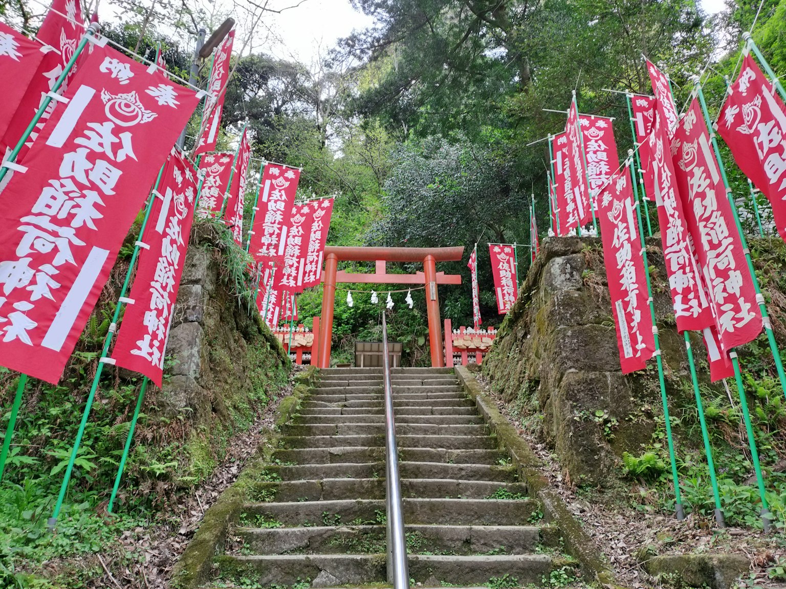 Pemandangan indah tangga yang menuju gerbang torii dengan spanduk merah di samping