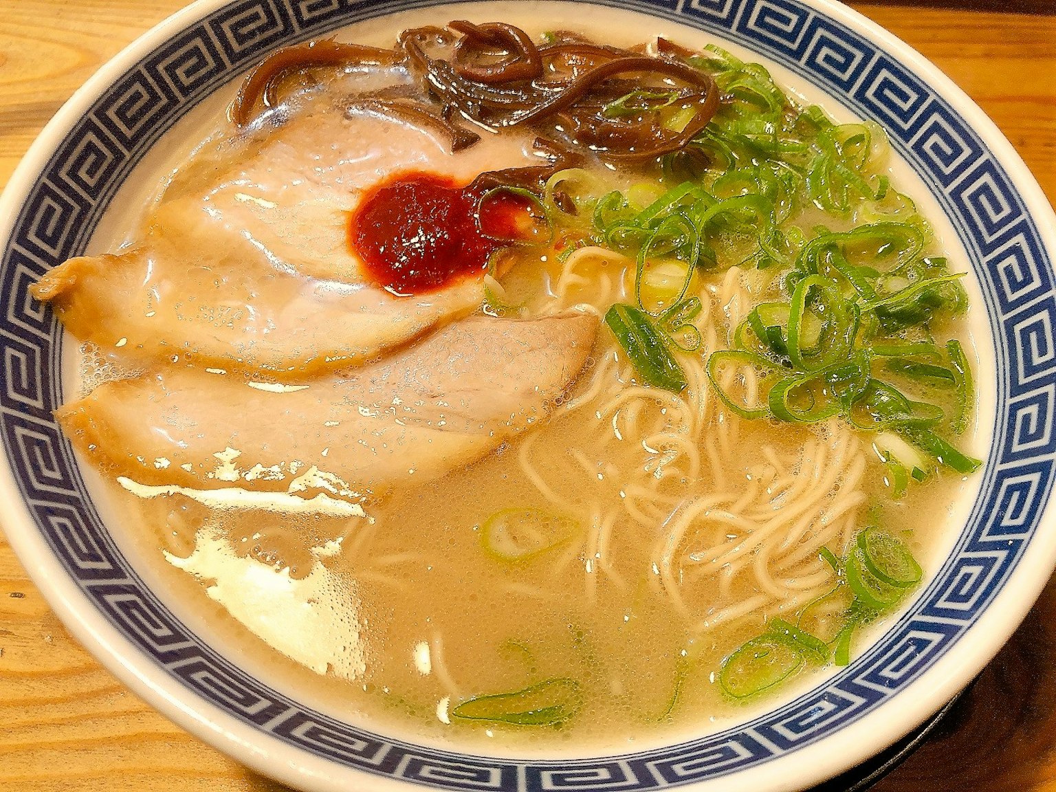 Mangkuk ramen dengan irisan daging babi, daun bawang, dan bumbu merah