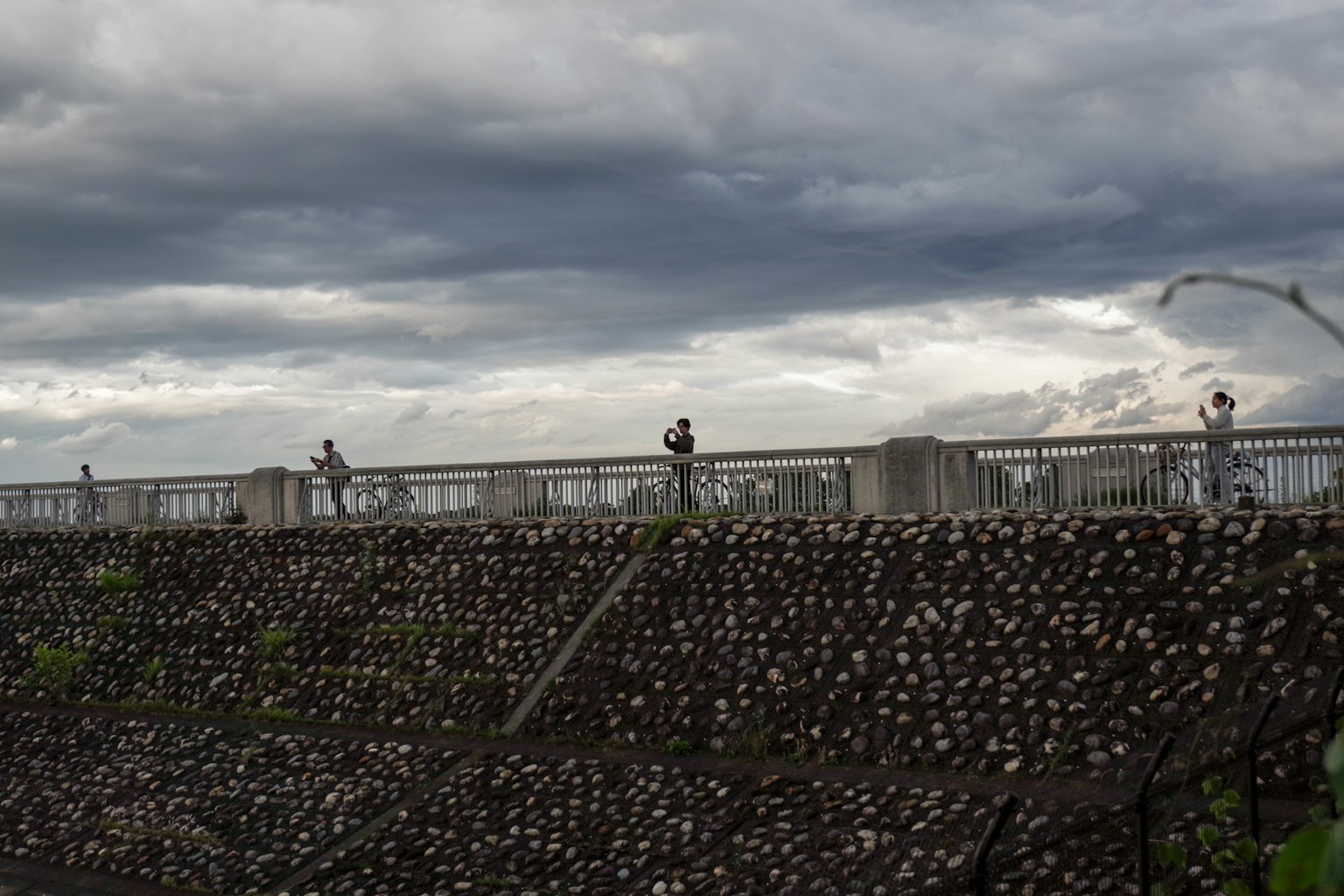 Personas de pie sobre un muro de piedra bajo un cielo nublado