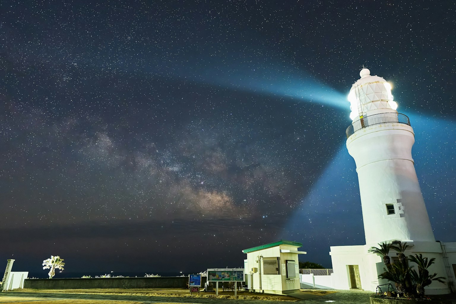Lighthouse under a starry sky with beams of light