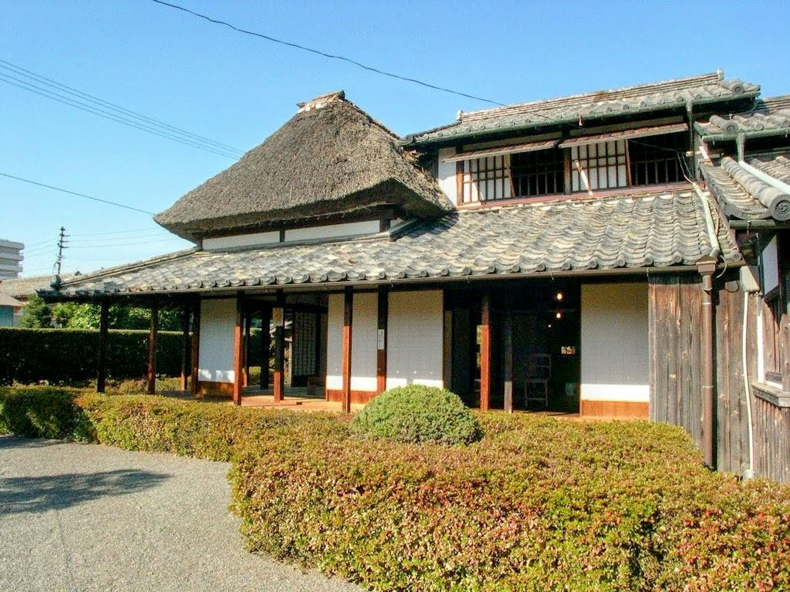 Eksterior rumah tradisional Jepang dengan atap jerami dan struktur kayu dikelilingi taman yang terawat