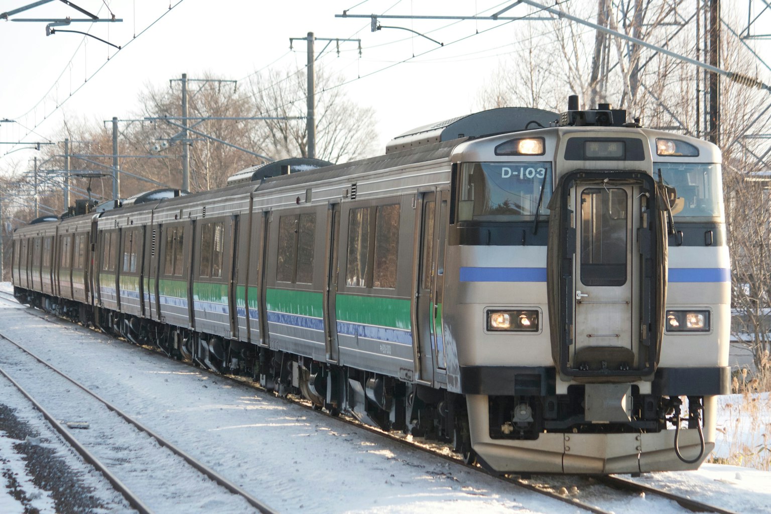 Train traveling on snowy tracks with a green stripe